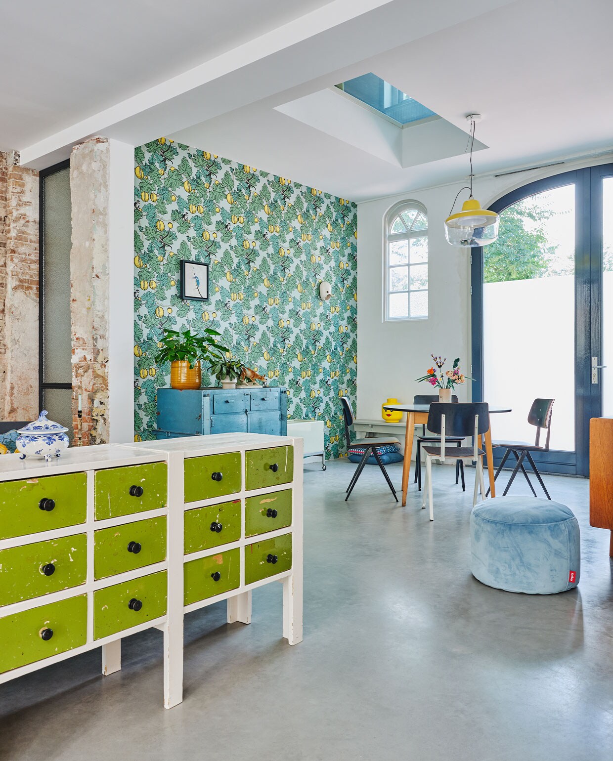 Behang Fornasetti Frutto Proibito van Cole &amp; Son. Wit-groen dressoir, blauwe kast en ronde eettafel vintage. Eetkamerstoelen S16 Galvanitas. Hanglamp Favourite Things via Eno Studio. Wandlampje The Party Kranen &amp; Gille voor Moooi. Voorraadpot Lego. Poef Fatboy. Overig onbekend.
