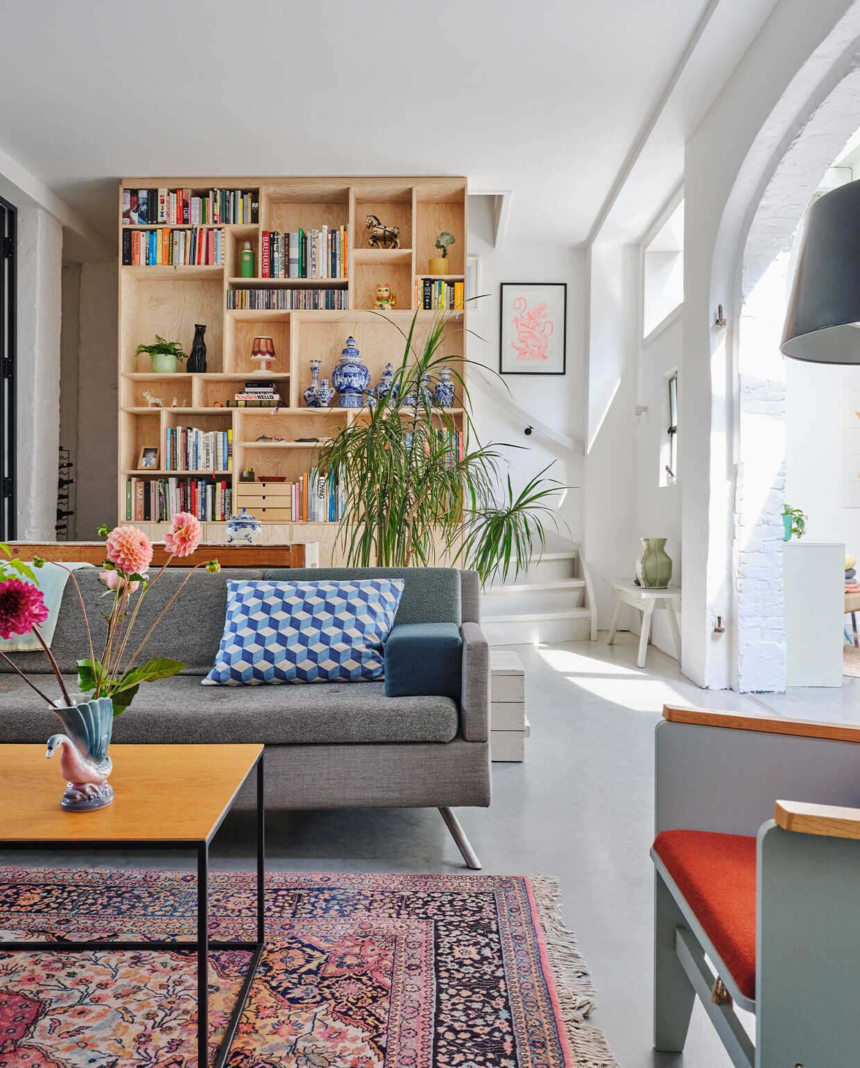 Bank Lot Studio Parade via Vrienden. Geometrisch kussen OXO. Salontafel eigen ontwerp. Fauteuil Katrijn van Floris Hovers via Vrienden. Vloerkleed vintage. Kastenwand op maat gemaakt van Pools grenenhout. Ingelijste prent Trobbies. Wit bankje Piet Hein Eek met daarop de Carter Vase van Floris Hovers via Cor Unum. Overig onbekend.
