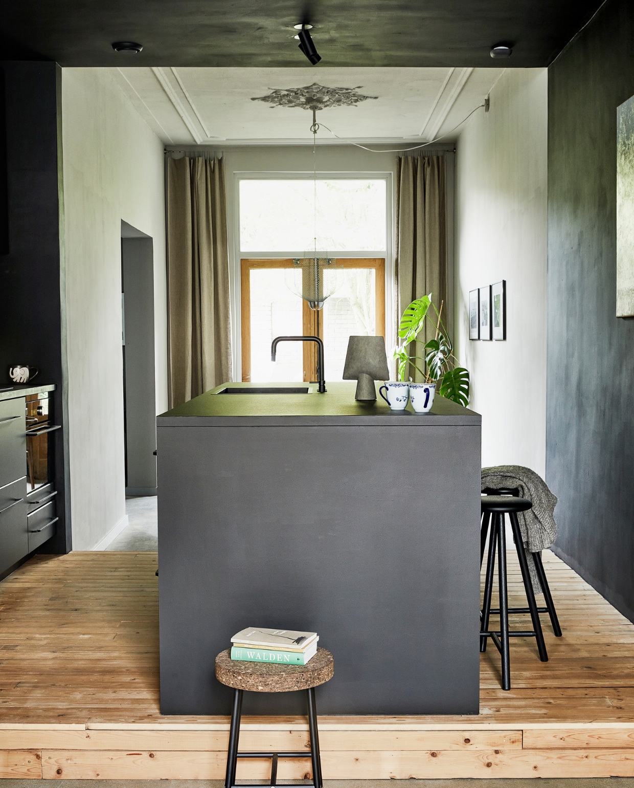 Verfkleur achterkamer Pavilion Gray en keuken Pitch Black van Farrow &amp; Ball. Plafondspot C1B Nosta Victor. Keuken en apparatuur Ikea (fronten Kungsbacka, grepen Borghamn). Werkblad bekleed met Desktop Linoleum Forbo. Kraan Nivito. Vaas Sphere Vase Square 101 Copenhagen. Kopjes Ostindia Rörstrand erfstuk. Barkruk Perch Nikari. Krukje Sinnerlig Ikea. Oude vloerdelen van Destijdsch.