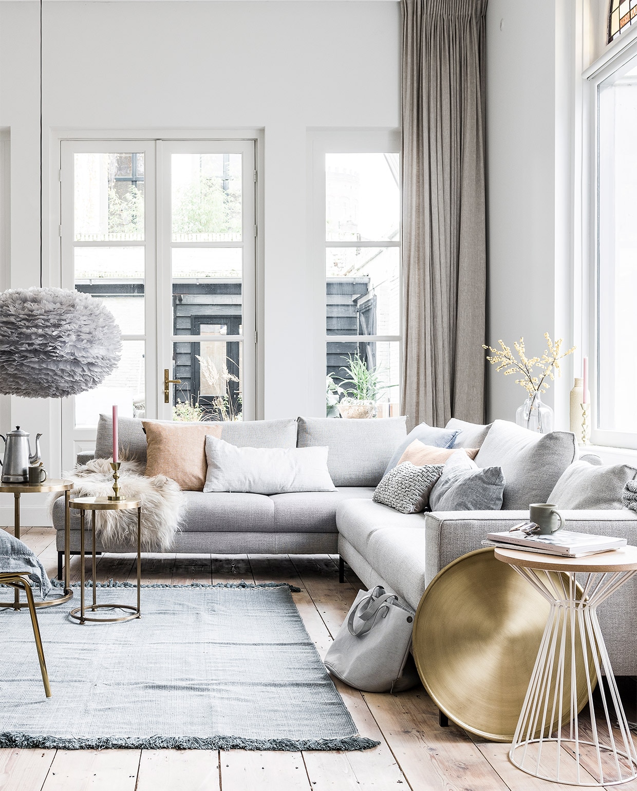 Hoekbank Aikon Lounge van Designonstock 2x 62x246x102 cm (hxbxd) € 3298,-, wit draadwerk tafeltje € 159,- (Eijerkamp). Schapenvacht krul € 99,- (Het Kabinet). Linnen kussens in zachte pastellen van By Mölle € 69,95, goudkleurige draadwerk loungestoel Mesh van Bloomingville € 469,- (vtwonen.nl). Blauw fluwelen kussen € 19,95 (Goround Interior). Grijs kussentje met lusjes € 24,99, grijze tas van Zuss € 44,95 (Nijhof). Grijze deken met gerstekorreldessin € 49,95, kandelaar groot € 19,99, kandelaar klein € 14,99 (H&amp;M). Brass tafeltjes Alex per set van 2 € 199,-, blauw chambrey kussen van vtwonen, 60×60 cm € 44,95, goudkleurig dienblad Brass € 27,50 (Het Kabinet). Vloerkleed Mekong Nights Stonewash Blue L, 160×230 cm € 229,- (aaimadewithlove.com). Hanglamp Eos van grijze veertjes € 399,-, kopjes per stuk € 7,95 (Nijhof). Lijst met foto van kind gemaakt door fotografe Linelle Deunk. Koffiekan en glazen vaas privébezit.