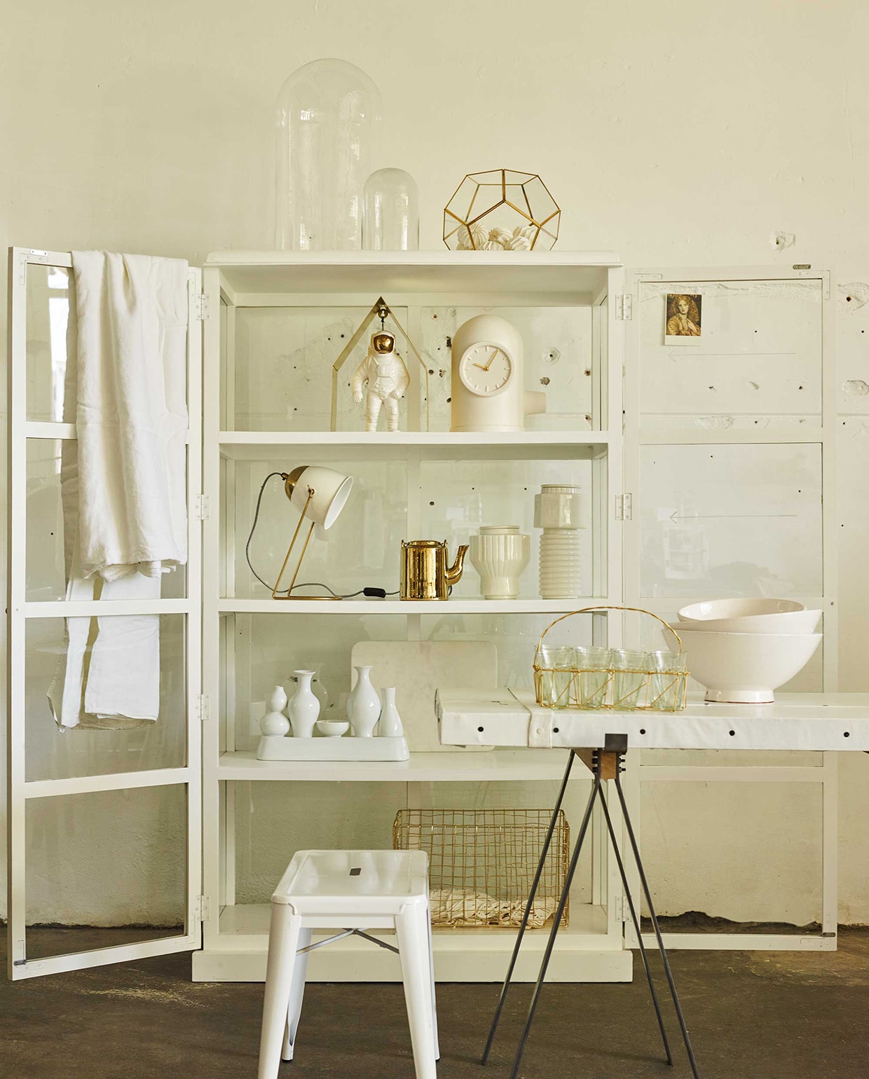 Vitrinekast, kruk, glazen stolpen (Portrait). Glazen windlicht facet met goudkleurige randen, papieren bollenslinger (Nordal). Schragen (Van Mokum). Tafelblad (Combitex). Op tafel: schalen (Household Hardware). Draadmandje met glazen van Madam Stoltz (Deens). In de kast: gouden huisje, vazen met ribbels van Diesel (Nijhof). Astronaut, klokvaas (Van Mokum). Lamp van Madam Stoltz, marmeren snijplank van Madam Stoltz (Deens). Theepot, vazen-vaas (Pols Potten). Draadstalen mand (Portrait), linnen kleed, gehaakt hesje (H&amp;M).