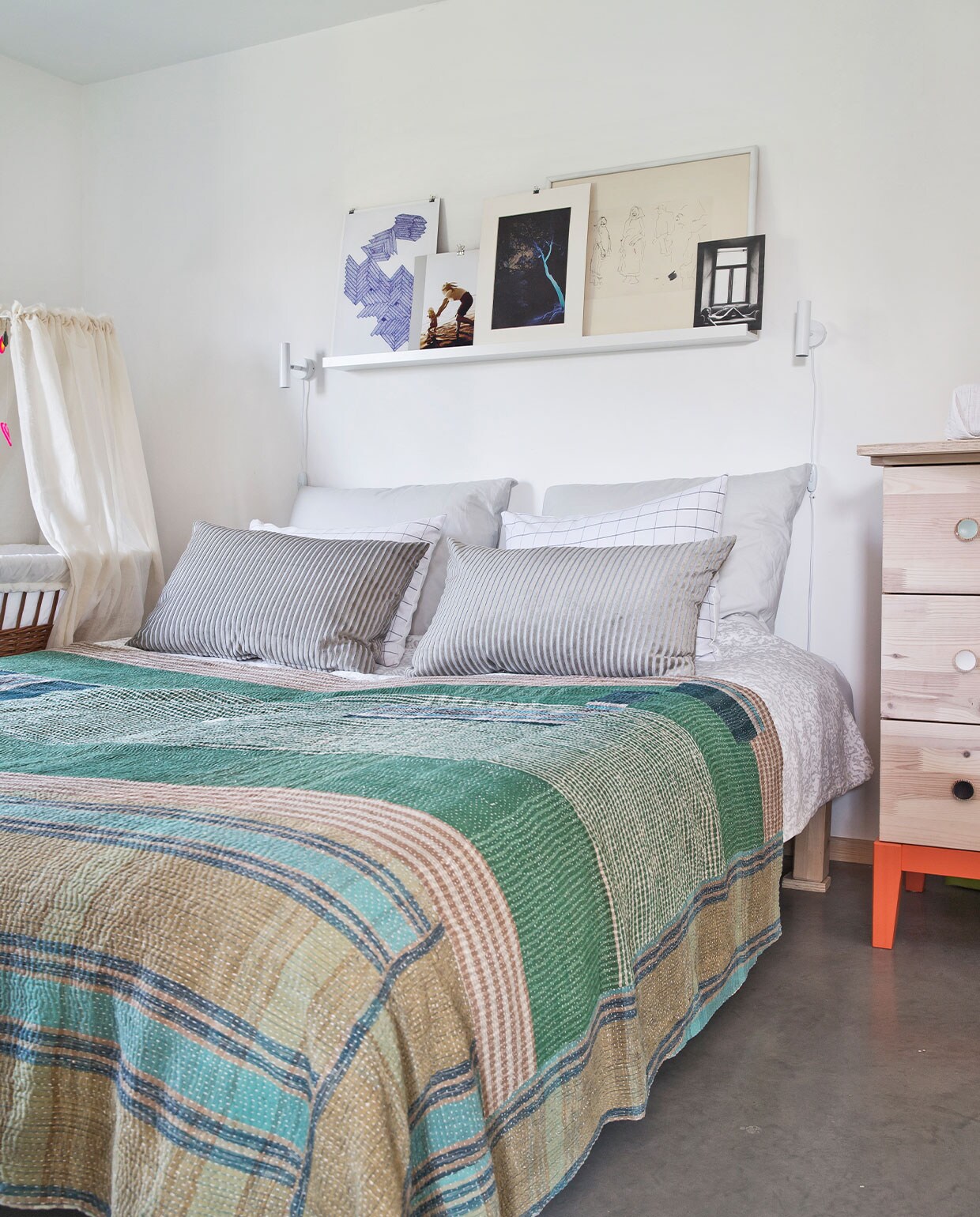 Bed en ladekast Ikea. Beddengoed Hay. Wieg kringloop. Bedlampjes Nordlux. Wandplank Ikea, daarop een mix van ingelijst eigen werk en brocantevondsten.
