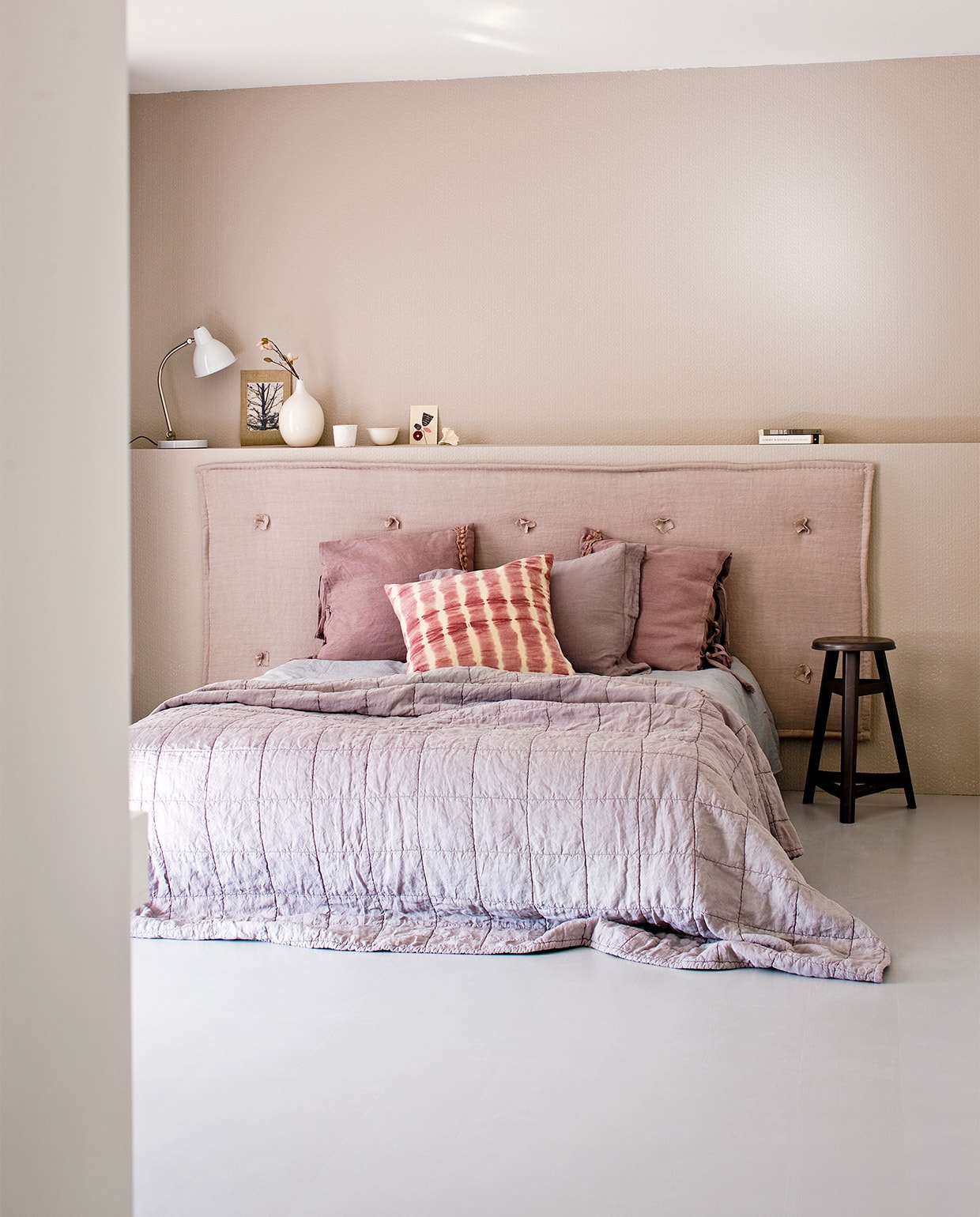 Uit de vtwonen huiscollectie: overschilderbaar behang Knitty per rol € 27,95, witte leeslamp € 299,-, roze tie-dye kussen 60×60 cm € 39,95, witte vaas € 14,95 oudroze linnen kussen met striksluiting € 44,95. Stof gebruikt voor hoofdbord Stonewashed (Chivasso). Kleur op behang: Elephant’s Breath (Farrow &amp; Ball). Overig privébezit