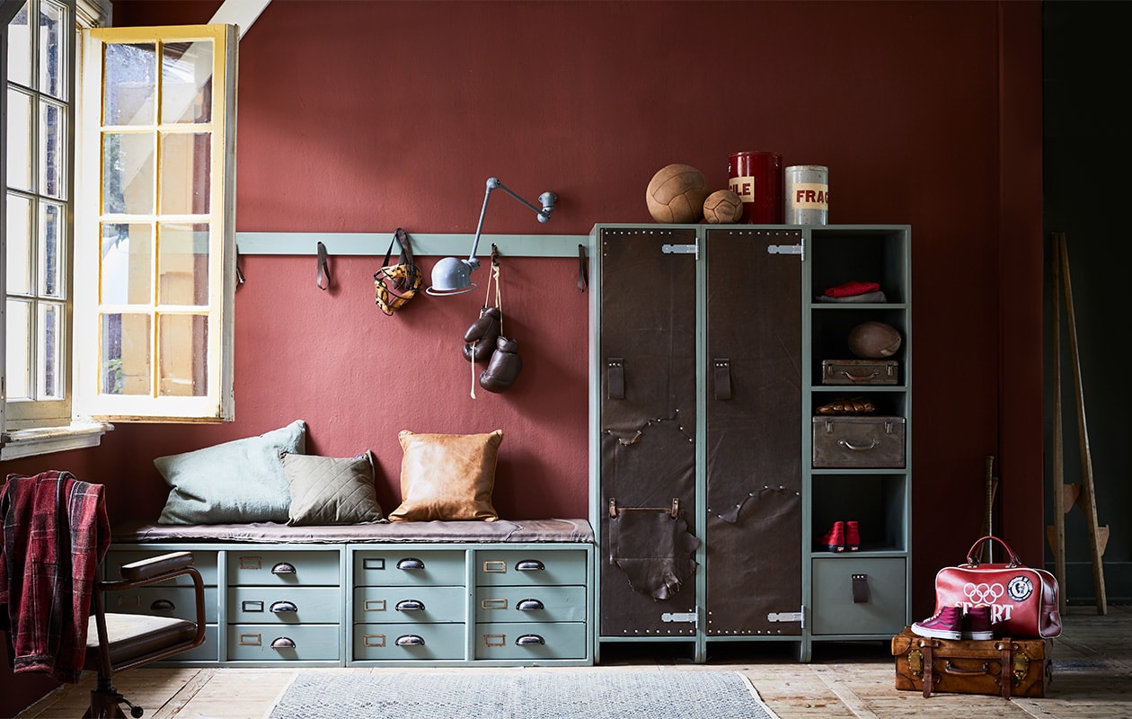 Op de wand muurverf in kleur Cardinal Red van Pure &amp; Original per liter € 37,20 (De Ru). Kast met met leer beklede deuren, 110x170x50 cm (bxhxd) € 775,-, lage kast met lades en leren kussen, 180x50x45 cm (bxdxh) € 375,-, plat leren kussen € 175,-, kapstok € 115,-, alles op maat gemaakt (Combitex). Geverfd met lakverf in kleur Cardroom Green van Farrow &amp; Ball, per 0,75 liter € 42,- (De Ru). Bokshandschoenen € 55,-, sporttas € 65,-, metalen koffer vanaf € 32,50, leren ballen vanaf € 55,-, blikken Fragile € 32,-, stoel € 145,-, masker € 42,-, American football € 37,-, honkbalhandschoen € 35,- (Spoor 38). Oude Jieldé wandlamp € 395,-, leren koffer € 120,- (Brût Amsterdam). Leren kussen, 50×50 cm € 89,-, doorgestikt legergroen kussen, 50×50 cm € 24,50, groot groen kussen, 70×50 cm € 58,50, vloerkleed, 175×100 cm € 125,- (De Weldaad). Schoenen, geruit overhemd van Vans. Stelten privébezit.