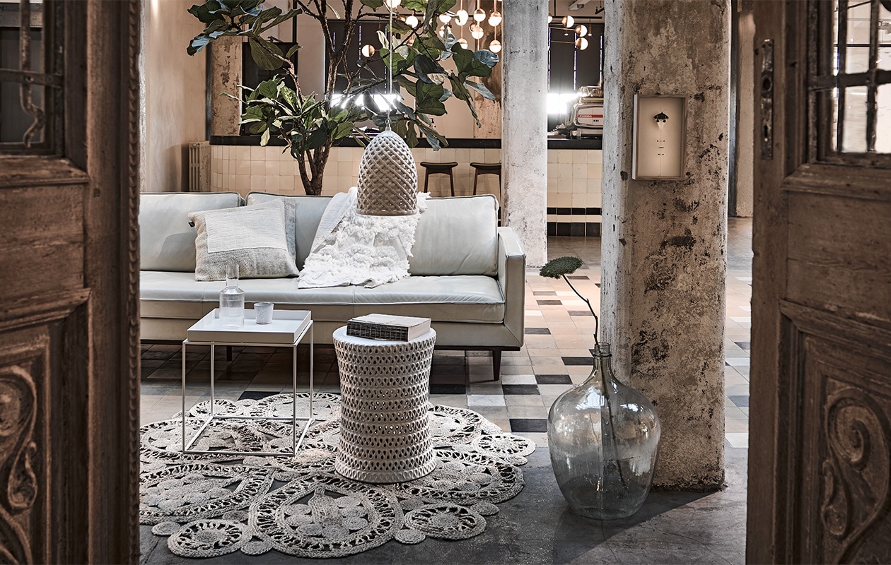 Antieke deuren per set van 2 € 895,- (burbriantiek). Witte leren 4,5-zitsbank Master, 286x96x86 cm (bxdxh) € 3394,- (loods5). Vloerkleed Ø 150 cm € 79,-(bepurehome.com). Kruk van keramiek € 195,-, hanglamp van keramiek € 195,- (polspotten). Glazen fles € 65,- (burbriantiek). Plaid € 49,50, kussen € 29,95 (hkliving). Kunstwerk aan de paal van Anne ten Donkelaar, prijs op aanvraag (anneten).