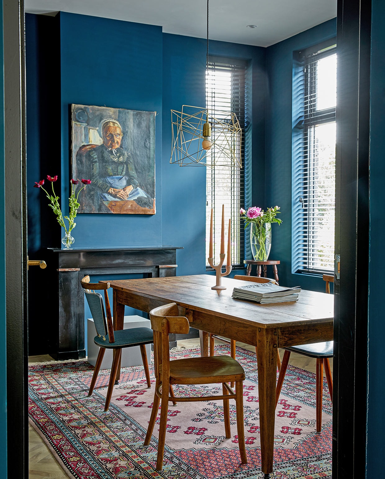Tafel en vaas op schouw vintage, stoelen en vloerkleed kringloopwinkel. Kruk uit de inboedel van het huis, vaas op de kruk Xenos. Raambekleding Jaloezieënfabriek Zuid, muurverf Haags Blauw van Farrow &amp; Ball, schilderij Marius Richters, lamp Wattnou.