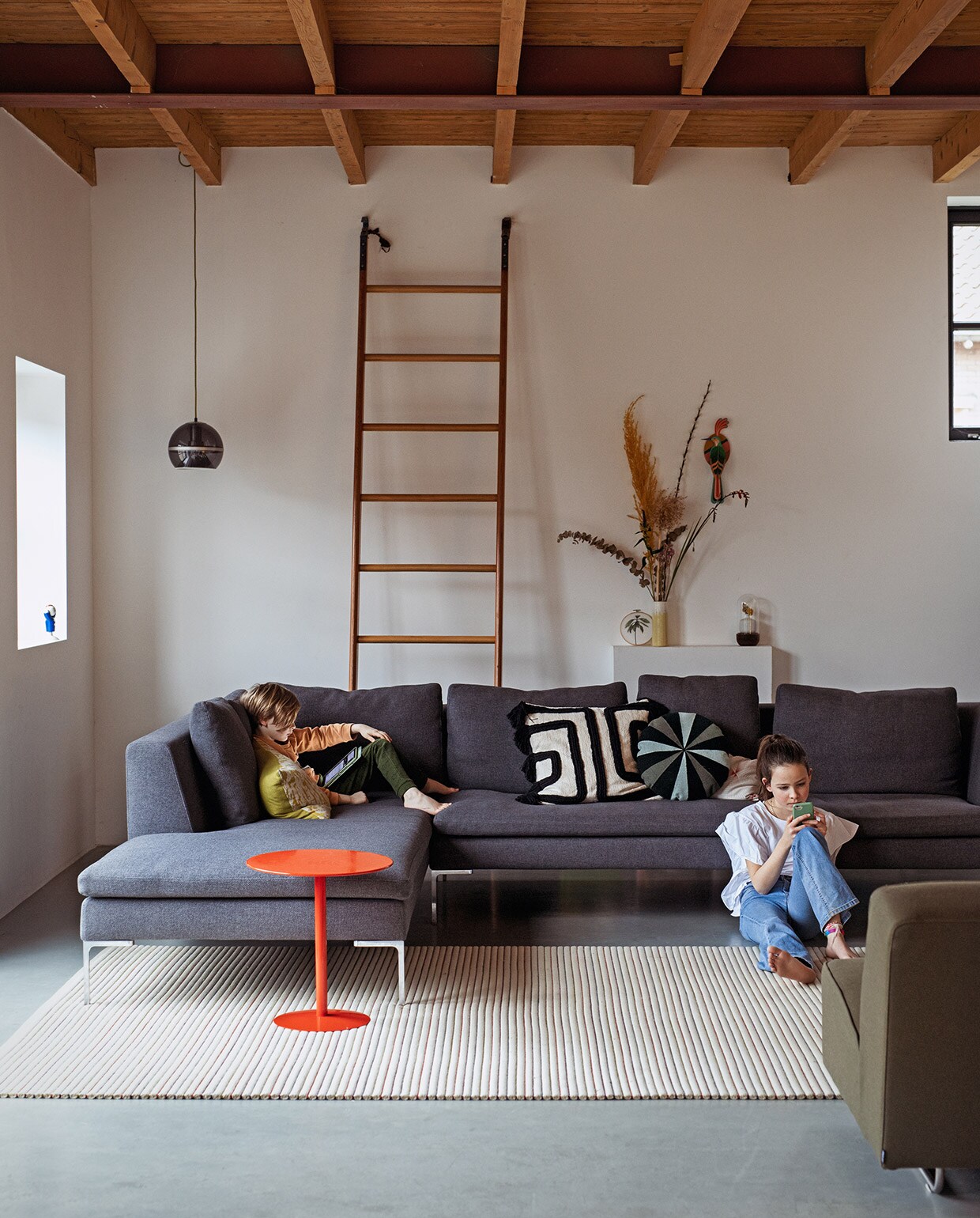 Bank Brechtje Olsthoorn Interiors, kussens zelfgemaakt, schapenvachtkussen Van Buren Bolsward. Groen linnen kussen, vazen, kandelaar, melkkruk, groene bijzettafel Sip &amp; Clara Pop-up Store. Tulp-tafel van Knoll erfstuk. Vintage kleed Richard Houpt Noordermarkt Amsterdam. Witte vintage bijzettafel B&amp;B Italia. Vintage buisframe stoel en wandlamp Marktplaats. Herkomst bronzen voorwerp onbekend. Aan de muur met de klok mee: tegel vogel uit Nieuw-Zeeland, groene deksel van ouderwets toilet, schilderij landschap rommelmarkt, horizonschilderij Auke van der Meulen, tegel uit Nieuw-Zeeland, aardewerken blad Trees In der Rieden, zeefdruk paardenbloem Ray Daal, grote foto cadeau gekregen, schilderij bomen kringloop.
