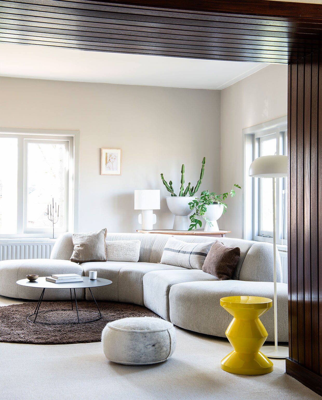 Bank HKliving. Crème kussen, kussen met streep van Ferm Living en witte tafellamp Anne-Marie Wonen. Wit, rechthoekig kussen Karwei. Bruin kussen Tell me more van Jet At Home. Salontafel en kandelaar K’willeminhuis via Anne-Marie Wonen. Vloerkleed Tapeso. Witte poef Jacobien Life &amp; Style. Bloempotten HKliving via Eijerkamp. Kunstwerk Tiny Stories. Gele kruk Zig Zag Pols Potten. Vloerlamp Ikea. Aardewerken kom op salontafel Muubs via Passie Wonen Soest. Mok Xenos.