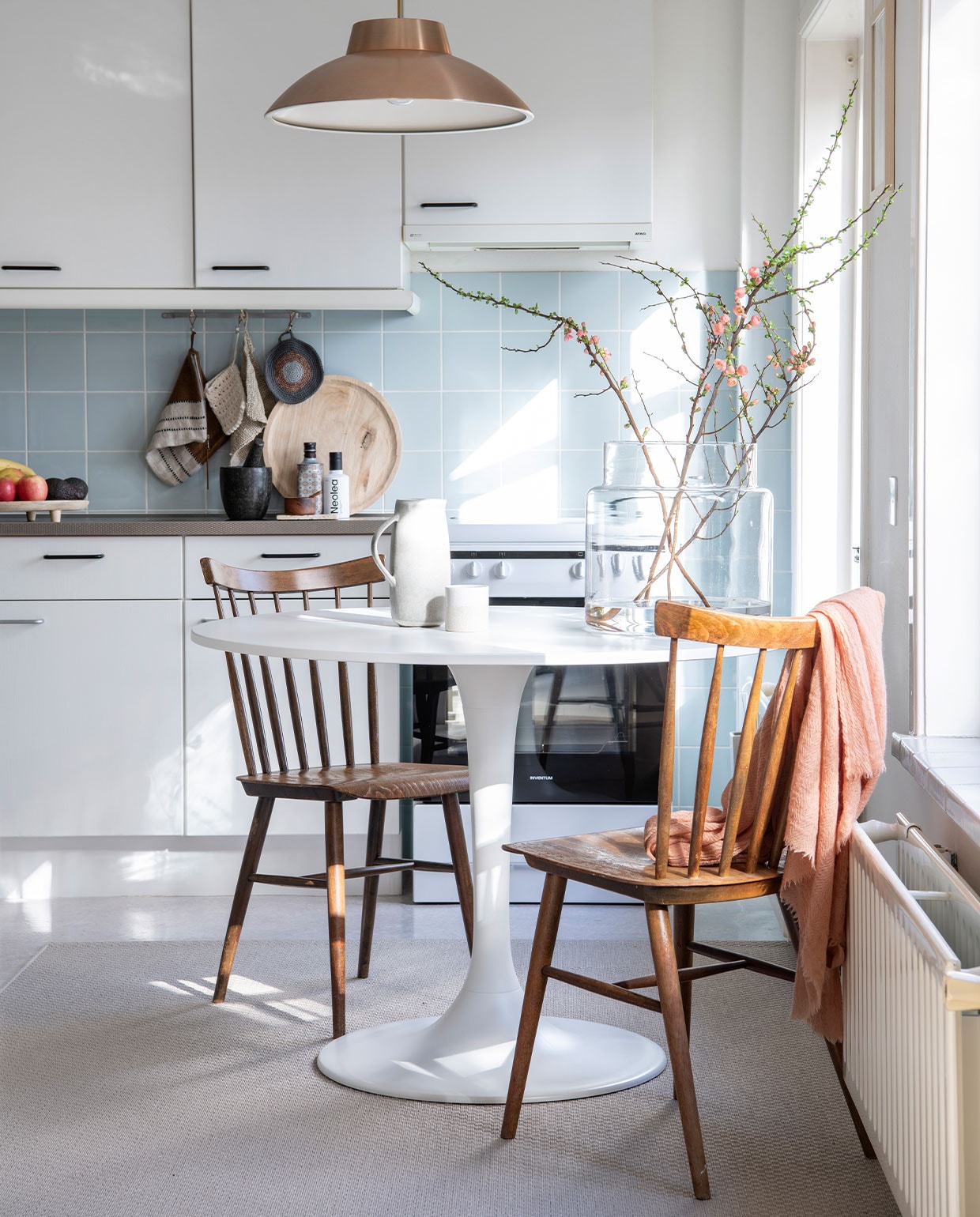 Muurverf RAL9016. Keuken en blauwe tegels uit de jaren zestig en marmoleumvloer zaten er al in. Witte kan en mok Muubs Anne-Marie Wonen. Vijzel en theedoek Blomus en fles rechts via Passie Koken &amp; Wonen. Fles links cadeau gekregen. Pannenlap rechts Far Wool, midden Lavinia Twee21. Houten dienblad Spijck. Vloerkleed en tafel Ikea. Roze sjaal Humanoid. Vaas en tak De Beleving Soest. Overig onbekend.