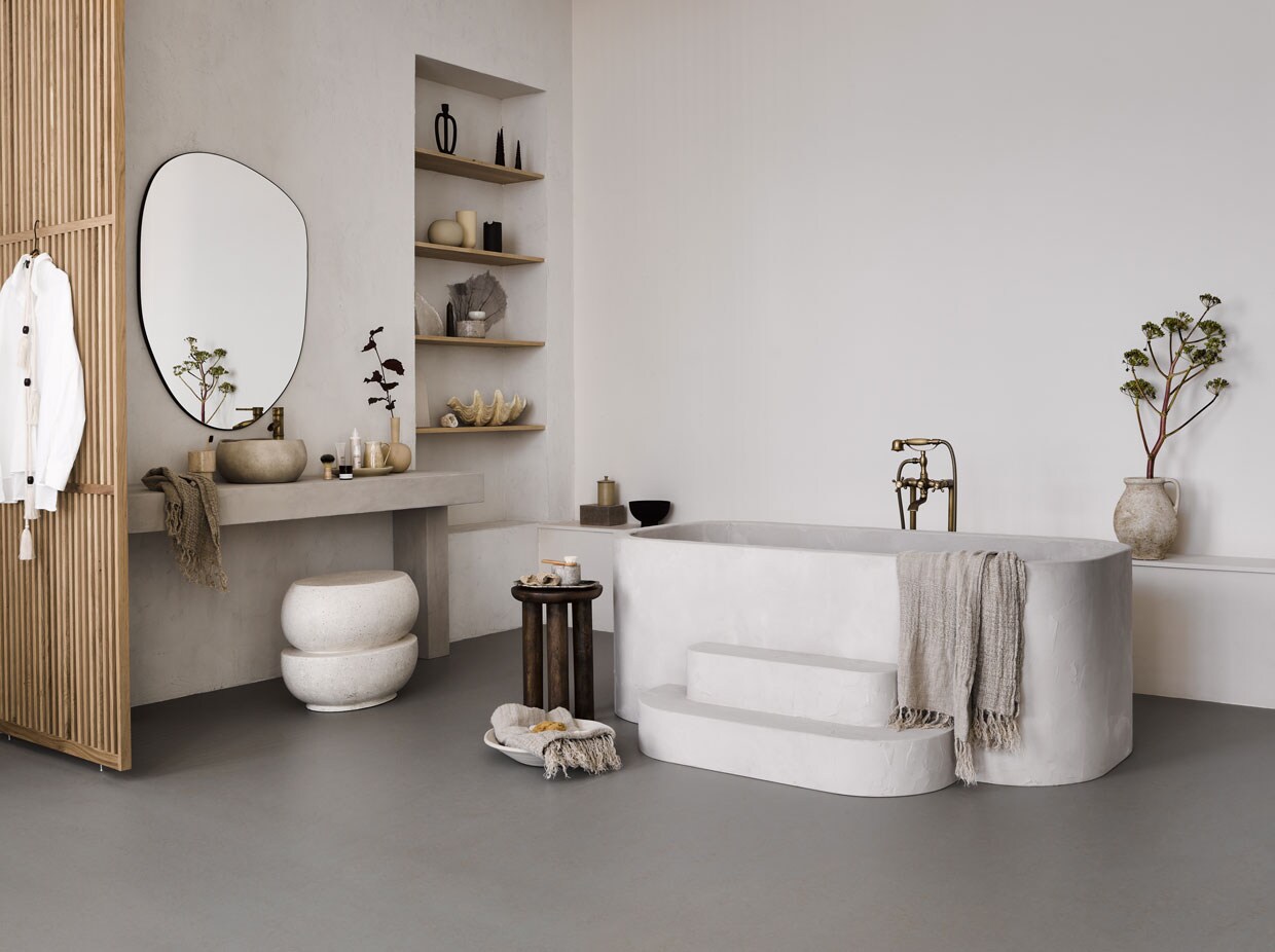 Marmoleum vloer kleur Lava. M.m.v. nordal.eu (bijzettafel, linnen handdoeken, marmeren potten, XL schelp, suède doos), lanena-home.com (microcement kruk), zarahome.com (spiegel, schaal, grote kan), bungalow.dk (schaal), byjoa.nl (zwarte kan, crèmekleurige vaas op plank). Overig privébezit.
