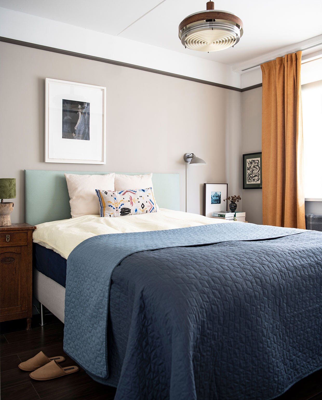 Muurverf Rolling Fog 143 en rand muurverf Attic II van Little Greene. Bed Ikea, hoofdbord van bed zelfgemaakt, dekbedovertrek Crisp Sheets, sprei Jysk, kussen Sissy-Boy Homeland. Nachtkast erfstuk, groene bedlamp Loods 5, grijze lamp Made. Kunst boven het bed van Dieuwke Spaans, zwart-witte kunst rechts van het bed van Piet van Stuivenberg, kunst op nachtkast rechts Sometimes people disappear van Guy Vording. Overig onbekend.