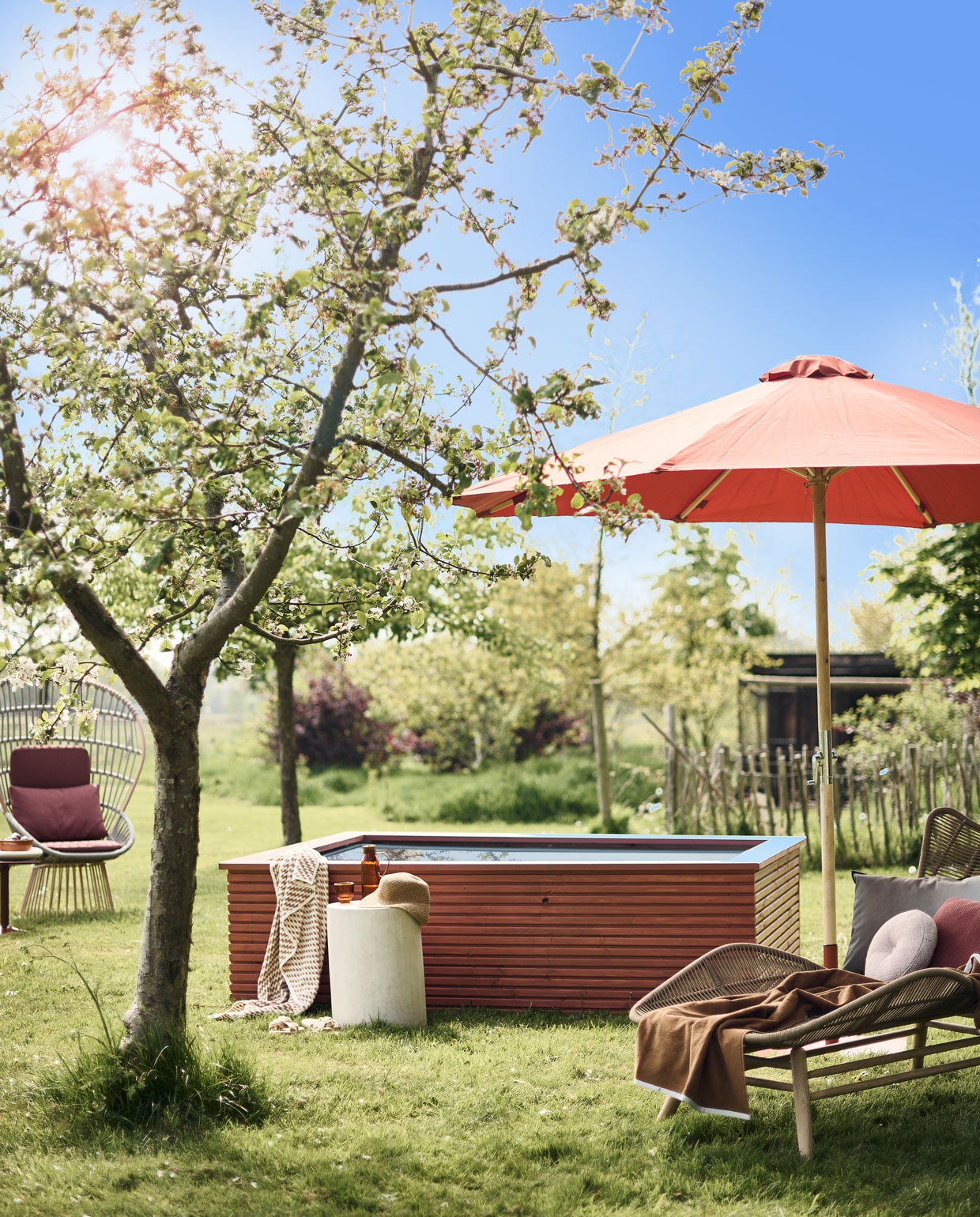 Ombouw zwembad DIY-project, geschilderd met Traditional Paint in kleur Dry Terra, per liter € 59,40 (pure-original.nl). Gepoedercoat aluminium fauteuil van Kettal € 3307,-, bijzettafel van B&amp;b Italia, steen en staal, 44,5×40 cm (hxØ) € 1019,-, zachtroze rond buitenkussen vanaf € 410,- terra rechthoekig buitenkussen € 151,- (dacks.nl). Katoenen handdoek met gele print € 29,99, hoed € 22,99, bruine katoenen badhanddoek € 22,99 (zarahome.com). Microcementen kruk vanaf € 449,- (lanena-home.com). Waterglas € 5,99, karaf € 21,99 (sissy-boy.com). Parasol en parasolvoet, hout, staal en polyester, 260×300 cm (hxØ) € 219,- (lanterfant.eu). Ligbed van Kave Home, houten frame met polyester zitting, 91x84x169 cm (hxbxl) € 667,- (vtwonen.be). Buitenkussen Padua van Designers Guild € 80,- (wva.nl).