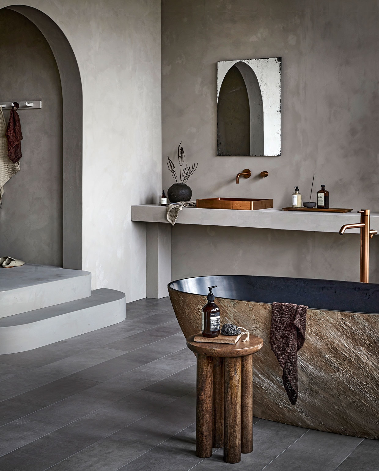 EVC-vloer Pebble, per m² € 63,99M.m.v. pure-original.nl (muurverf Fresco in kleur Soft Taupe), filiaal4.nl (bad, wastafel in Copper, wastafelkraan en badkraan Slimline in Brons), nordal.eu (houten bijzettafel, handdoeken), letoile.store (stenen onderzetter, handzeep, wierookhouder, wierook), paviljoennoord.com (spiegel), zarahome.com (slippers, grijze handdoek, vaas, houten dienblad). Overig privébezit.