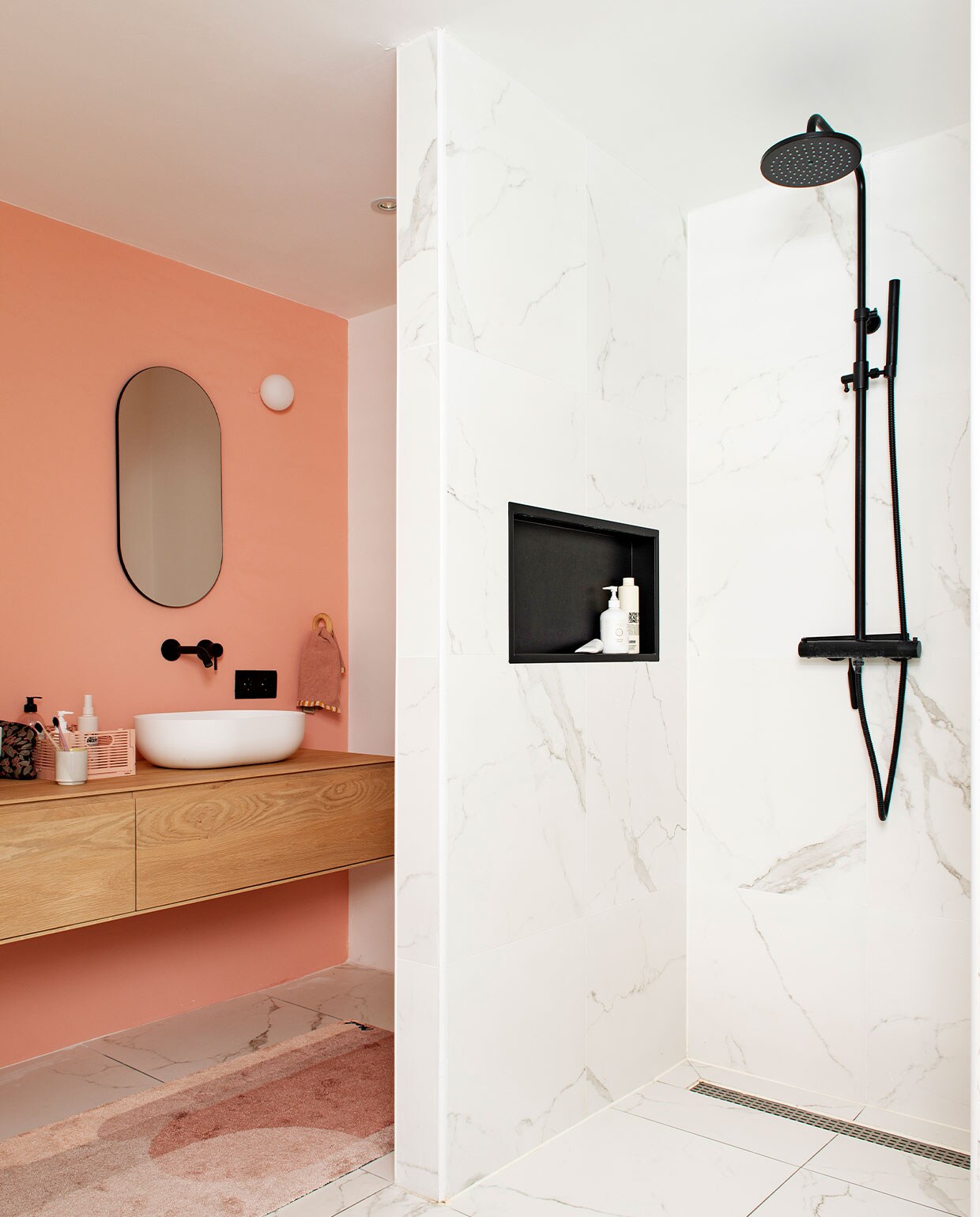 Muurverf Subtle Red van Flexa. Marmeren tegels Tegelmegashop. Wastafelmeubel en wasbak Houtmerk. Kranen en douchegarnituur Saqu. Spiegel House Doctor. Wandlamp Flos. Badmat Mad About Mats.
