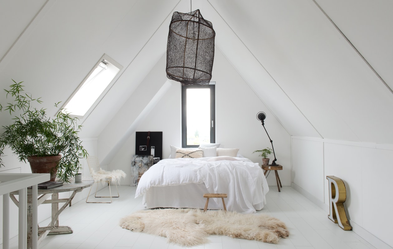 De ouderslaapkamer is licht en wit en ingericht met veel vintage. Hanglamp Ay lluminate. Bertoia Chair met vilten vacht van Marktplaats. Voor het bed vilten schapenvacht, Marktplaats. Houten krukje Van Hees Design. Kussen bed Souks. Bedlinnen By Molle. Zwarte lamp Jieldé. Vintage krukje als nachtkastje. Krijtbord vtwonen. Links: oude wijnklaptafel Park99. Vintage lichtletter van rommelmarkt.