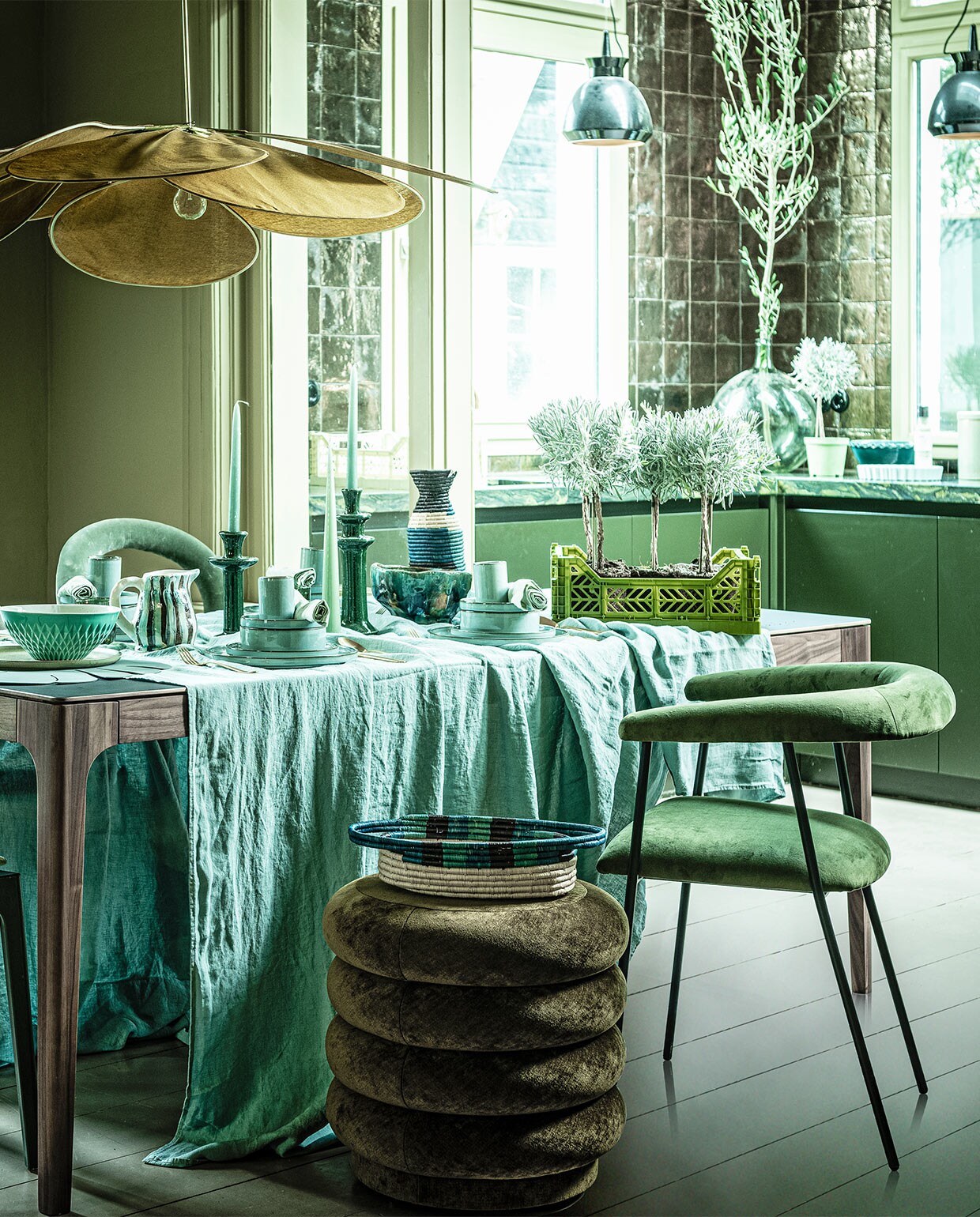 Groene eetkamerstoel, , Tafel Rikke walnoot met Fenix blad, 160x90x76 cm (demachinekamer.nl). Poef (fermliving.com). Velours stoel links Gubi Beetle, glazen fles op trolley (homestede.nl). Velours stoel rechtsachter (covanderhorst.nl). Houten stoel Bliss van Woood, velours stoel rechtsvoor Haily van Dutchbone, trolley Mil van Dutchbone, rond bord Surface van Serax, per 4, ovaal tapasbord Surface van Serax, braadpan Surface van Serax, water­glazen Raami van Iitala, per 2, goudkleurig bestek Amefa vintage 24-delig, taartvorm tarte tatin van Jamie Oliver (vtwonen.be). Wijnglas op trolley (zarahome.com). Waterflessen, krat klein prijs op aanvraag, krat groot, kan gestreept, kandelaars en kaarsen prijs op aanvraag, opgestapeld: kopjes klein, per stuk, borden, schaaltjes middel, per stuk, groenblauwe gevlekte schaal, voorraadpot prijs op aanvraag, groene schaal op keukenblad (loods5.nl). Linnen tafellaken, 320×270 cm, mand, hoge kan (couleurlocale.eu). Koffertje, lamp, Ø 120 cm (archive-store.nl). Kussen (hinck.nl). Linnen servetten, per 2 (hm.com). Grote vaas (oudebouwmaterialen.nl). Groene schaal op tafel (ottomania.nl). Placemat (bijenkorf.nl). Plantenpot (uncwardrobe.com). Schilderij Branch on a green canvas, 80×100 cm (maartjevandennoort.nl).