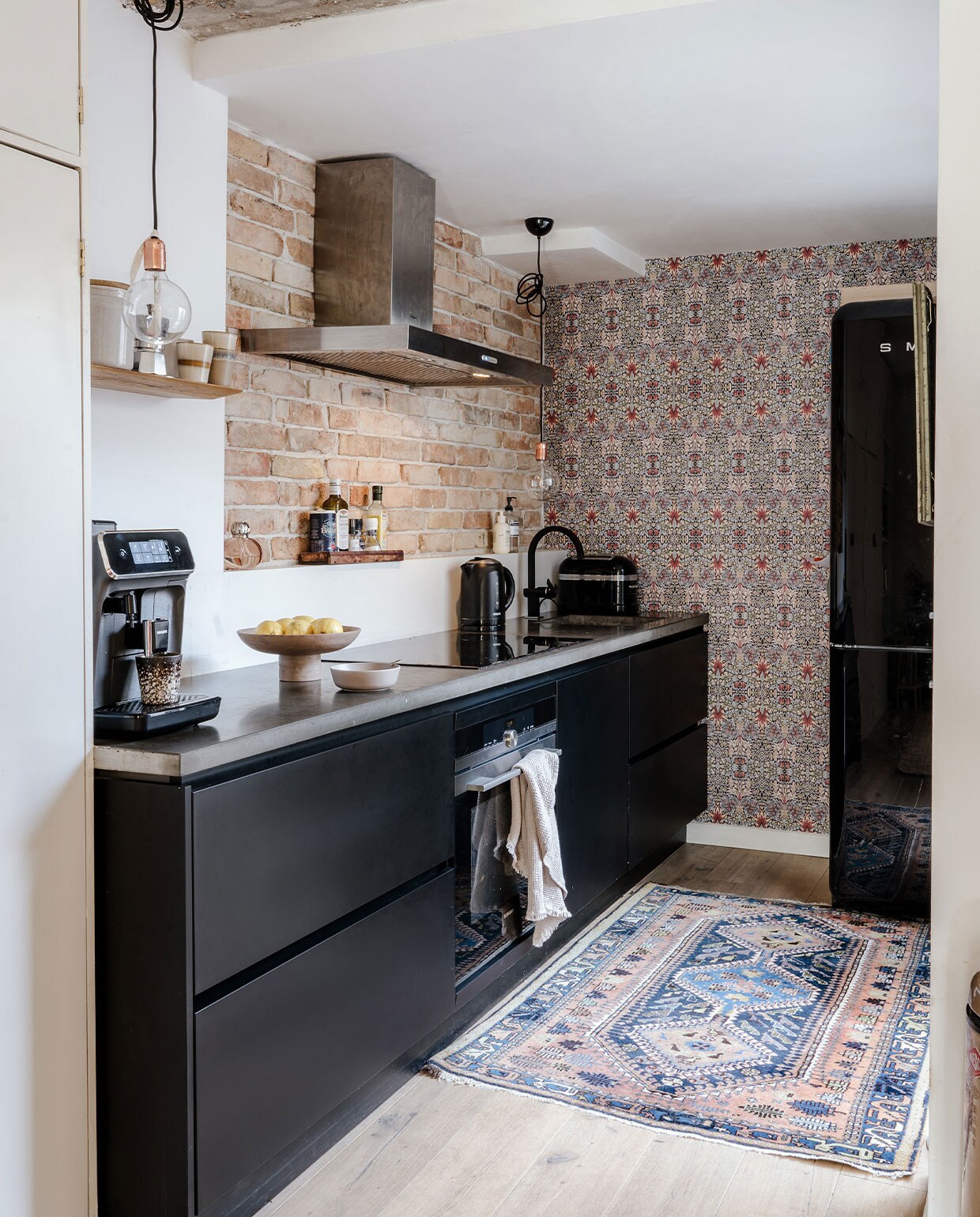 Behang Morris &amp; Co, houten vloer Basic Floors, kleed vintage, keuken Keukenloods, lampen zelfgemaakt, fitting Loods 5, theedoek en fruitschaal H&amp;M Home, koffiezetapparaat Philips, mokken HKliving, broodrooster KitchenAid, waterkoker Krups, koelkast Smeg, schaal By Lille Vilde, koekblik Hema, houten plank Sissy-Boy.