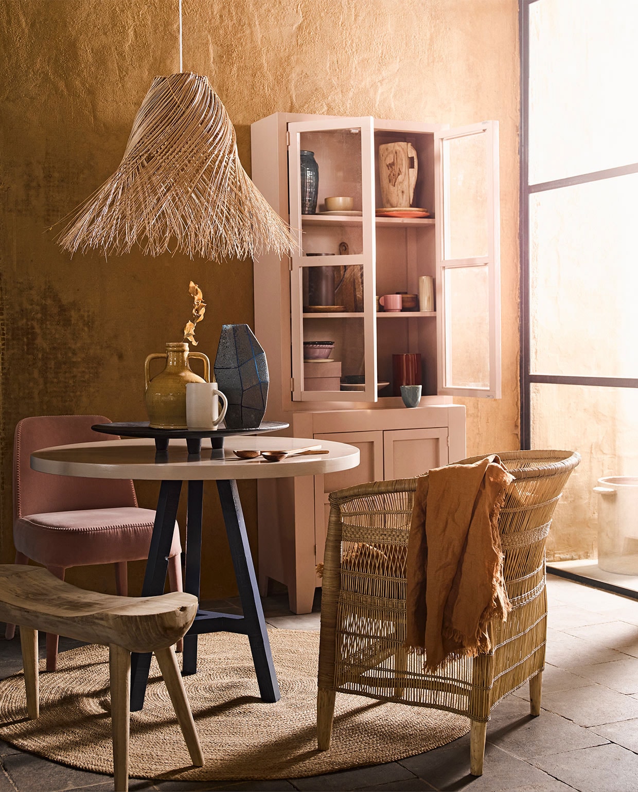 Ronde tafel met blauwe poot prijs op aanvraag, roze kast prijs op aanvraag (com-anders.nl). Hanglamp, gele vaas met oren, rond vloerkleed maat L, zwart dienblad, roze doos in kast, houten bord in kast, oranje bord in kast, bruin bord in kast, geel schaaltje, blauwe vaas linksboven in kast (loods5.nl). Bruin tafelkleed, snijplank, paarse kan, slabestek, bruin potje met deksel in kast, roze mok in kast prijs op aanvraag (hm.com). Blauwe mok, blauwe vaas op tafel (thingsilikethingsilove.com). Roze schaal op poot van HK Living (wonenmetlef.nl). Houten vaas in kast, paars schaaltje in kast links onder, lila schaaltje onder in kast (householdhardware.nl). Pot buiten, rode vaas in kast, beige vaas in kast middelste plank rechts (serax.com). Witte kan op tafel (annemiekebootsceramics.nl). Houten bankje van Mica links (vtwonen.nl). Roze stoel van stof (edha-interieur.nl). Stoel gevlochten hout (archive-store.nl).