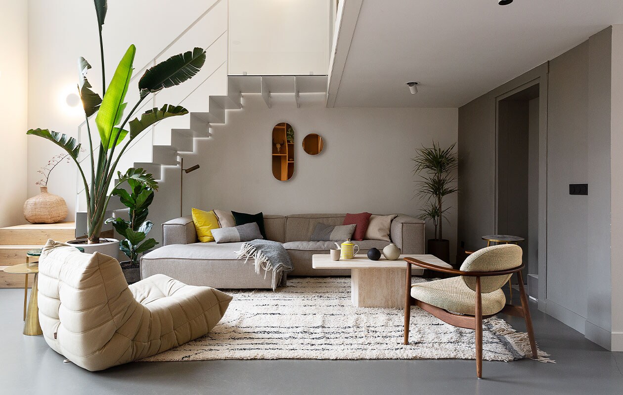 Metalen trap eigen ontwerp. Bank Dunbar van Fést, fauteuil Togo van Ligne Roset, stoel Roundy en serviesgoed Pols Potten, vintage salontafel via Marktplaats. Kleed Beni Ouarain uit Marrakech, spiegels Serax, plaid Evenaar. Ronde aardewerken vaas Pottery Pots, plantenbakken Ferm Living, planten Intratuin en 123planten. Messing bijzettafel HKliving, bijzettafel op hoge poten Pols Potten. Kussens HKliving en Pols Potten. Staande leeslamp Karwei. Plafondspots Spyder van Wever &amp; Ducré. Egalinevloer 2-componenten. Muurverf Ral 7030 van Fairf. Overig herkomst onbekend.