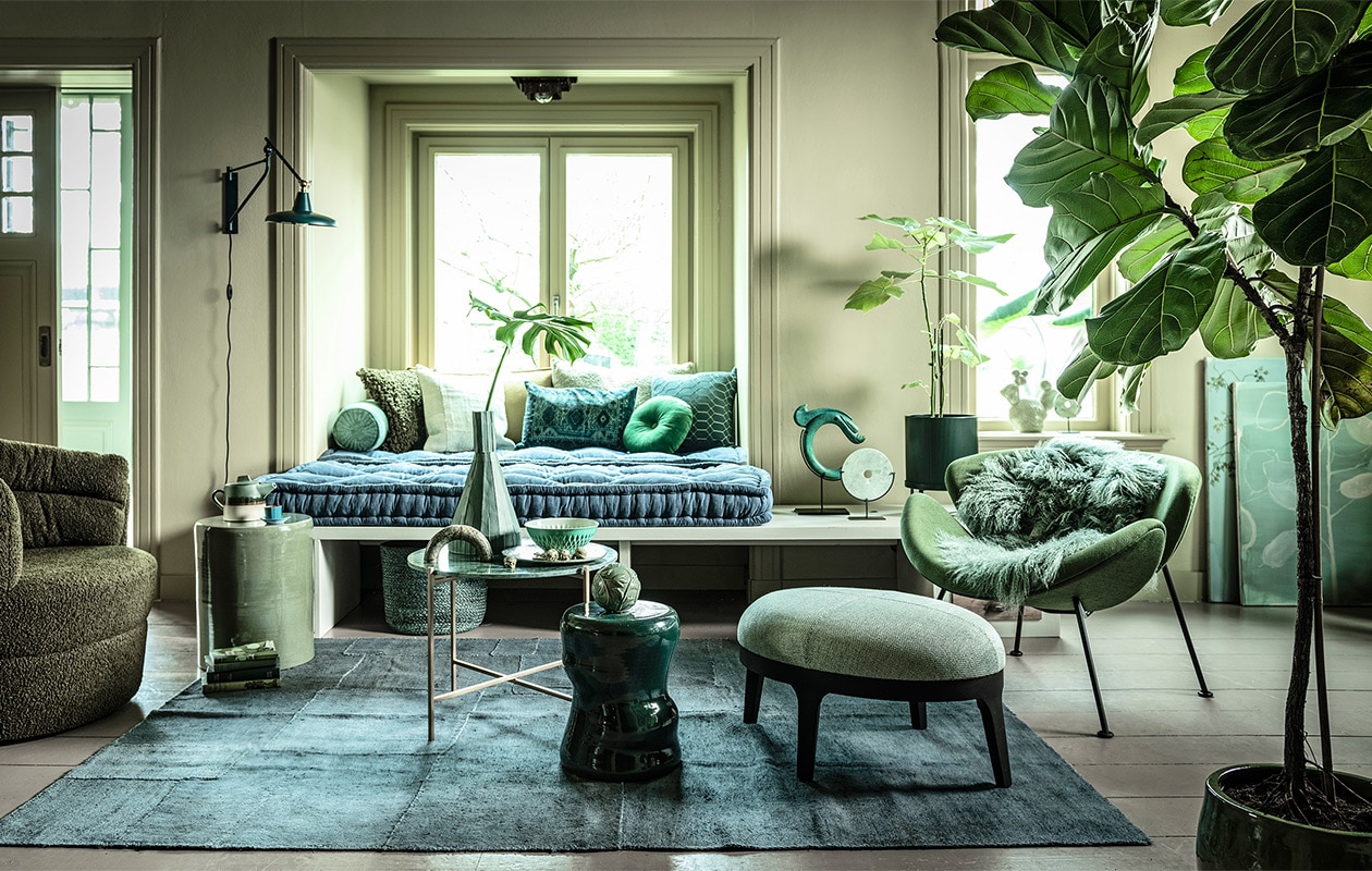 Fauteuil links (flinders.nl). Bank op maat gemaakt (com-anders.nl). Zitting bank twee stuks op maat gemaakt, 210×80 cm, geel/groen langwerpig kussen (coco-mat.com). Fauteuil Orange Slice van Artifort, cactus van Hay (homestede.nl). Marmeren tafel, kruk links, kruk midden, kussen langwerpig met oude opdruk, ronde sierbol op kruk prijs op aanvraag, sierobject draak (loods5.nl). Poef, grof kussen, kussen geometrisch (covanderhorst.nl). Marmeren sierobject op tafel (wonenmetlef.nl). Bord, per 6 (livingandcompany.com). Theepot (bijenkorf.nl). Vloerkleed, 242×178 cm, langwerpig kussen achter, lichtgroen kussen voor, mand (couleurlocale.eu). Wandlamp Hector van Dutchbone, rond kussen Mandarin van Kaat Amsterdam, Ø 40 cm (vtwonen.be). Notitieboeken (maisonnl.com). Espressokop en schotel schaal (ottomania.nl). Rolkussen (hinck.nl). Hoge vaas, ronde siervorm op bank en in vensterbank (badenbaden.nl). Schilderijen achter Branch on a green canvas, 80×100 cm, en Floral sketch, original painting, 70×80 cm prijs op aanvraag (maartjevandennoort.nl). Plantenpot op pootjes (fermliving.com). Plantenpot op grond uncwardrobe.com).