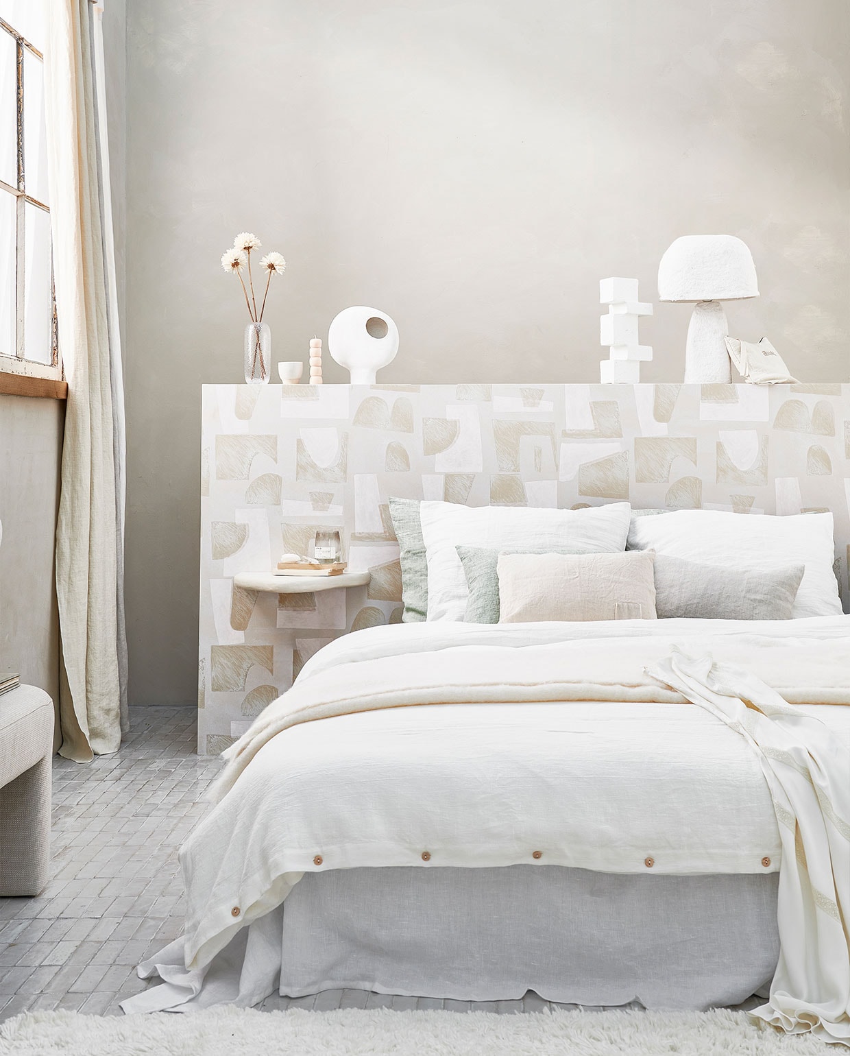 Muurverf in kleur Mallorca van We are Wowmakers, vanaf 2,5 liter € 110,- (fabriekzuidermeer.shop). Gestoffeerde bank van HKliving € 449,-, witte vaas van Be Pure Home € 45,30, vloerkleed van Linie Design € 715,-, wit blokornament van vtwonen € 35,25 (vtwonen.be). Gordijnen gemaakt van linnen stof Brera Lino van Designers Guild, per meter € 86,- (wva.nl). Hoofdbord behangen met behang Tutto uit collectie Voiles de Papier van Elitis, per rol € 196,- (loggerewilpower.com). Pleisterwerk wandplank € 90,-, grijs linnen sierkussen € 56,- (velv.nl). Glazen vaas € 24,- (bolia.com). Mok € 14,90 (letoile.store). Handgemaakte kaars, set van drie € 45,-, toilettas € 60,-, zandkleurig kussen met vierkant vlak € 69,- (sukha.nl). Witte keramieken vaas € 44,95 (urbannatureculture.com). Witte papier-maché tafellamp € 129,- (hm.com). Linnen laken in kleur Pure White, vanaf € 129,-, linnen dekbedovertrek in kleur Warm White, vanaf € 155,-, linnen kussenslopen in kleur Warm White en Sage, vanaf € 30,- (bymolle.com). Overig privébezit.