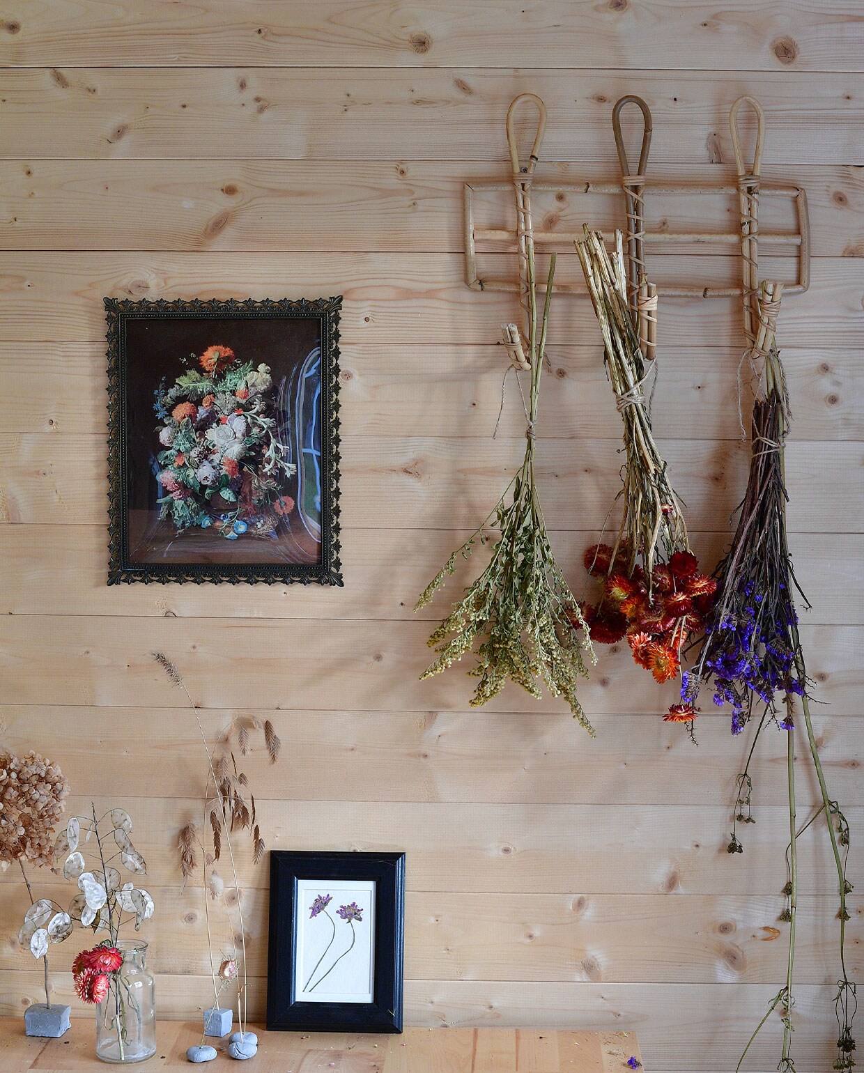 Aan een rieten kapstok van Dille &amp; Kamille hangen onder andere papierbloemen (midden) te drogen. Schilderij kringloop­winkel, gedroogde bloem in lijst zelf gedaan.