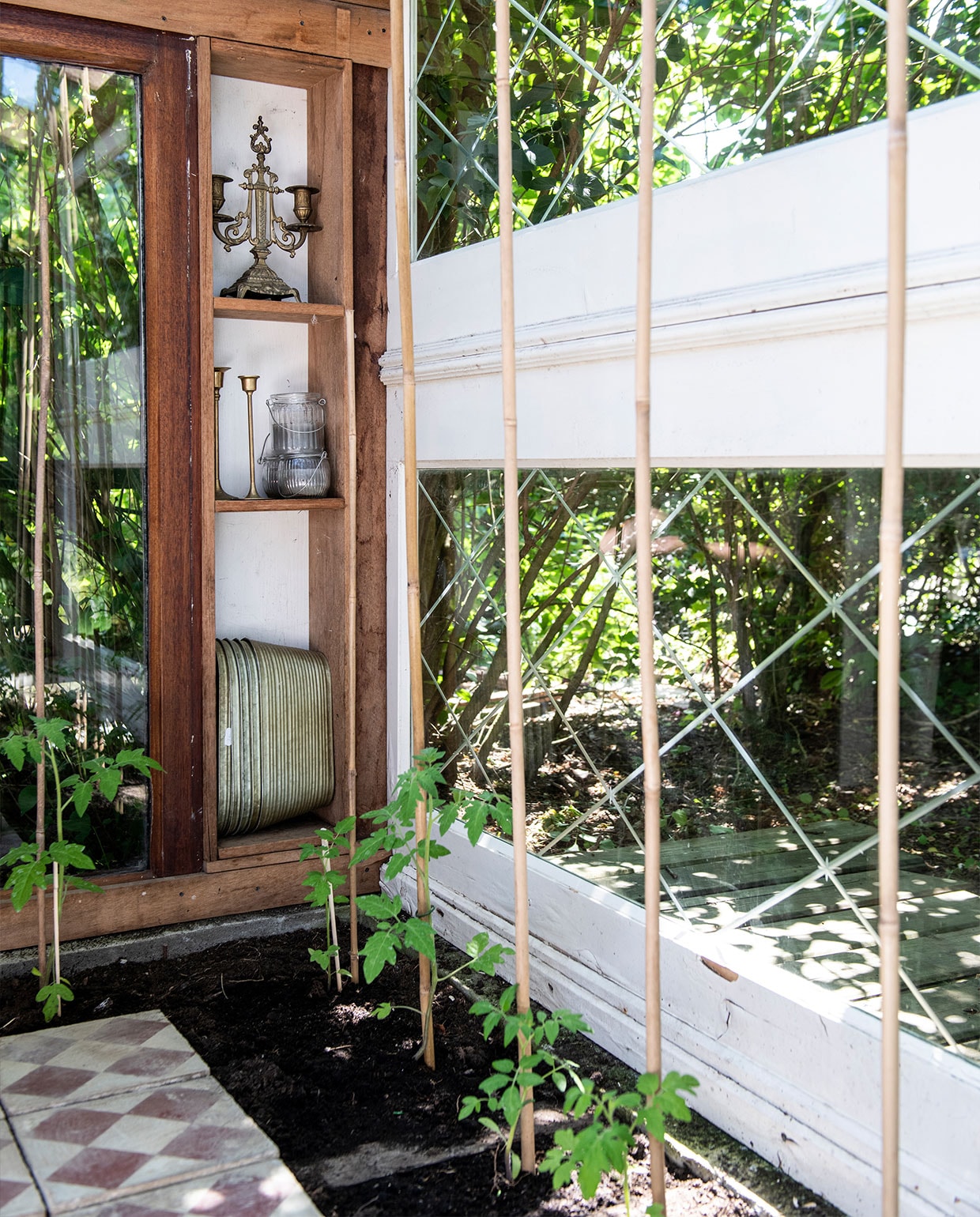 Martin maakte de kas zelf van onder andere gevonden en-suitedeuren. Kandelaren Van Manen aan Tafel, metalen plantenbakken Dickens-Style, tegels Kringloop De Driesprong Lisse. Tegen de bamboestokken groeien tomatenplanten.