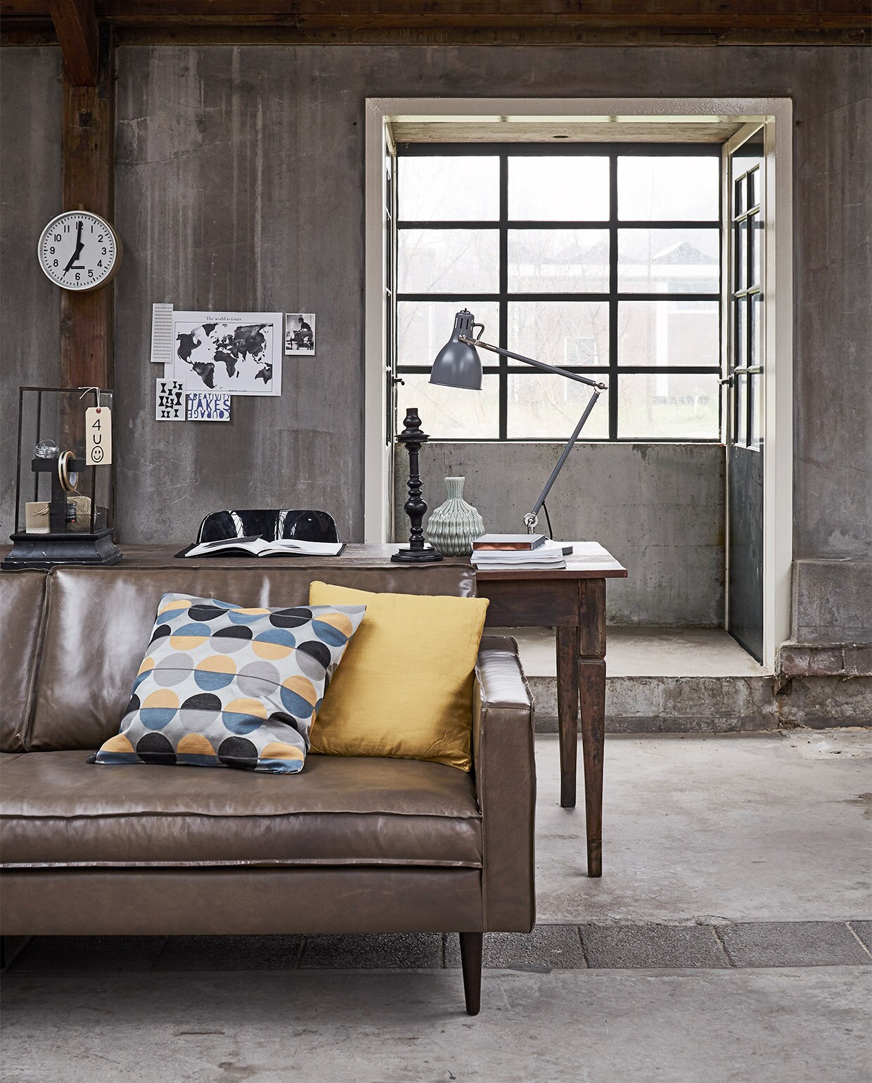 Oude teakhouten tafel, 200×90 cm (Jan van IJken Oude Bouwmaterialen). Bank Slimm in leer, kleur Fango, 78x96x211 cm (Design Loods 5). Zwarte Revolt stoel, 47x51x83 cm (bxdxh), klok, letter T in vitrinekast (Neef Louis). Vierkante stolp, 30x30x45 cm , kandelaar (De Weldaad). Groenige vaas (HK Living). Overig privébezit.