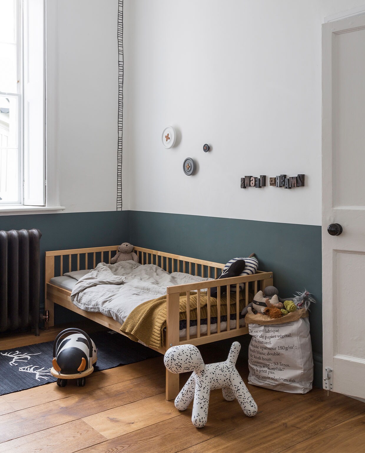 Muurverf lambrisering Estate Emulsion Inchyra Blue van Farrow &amp; Ball. Bed Ikea, dekbedovertrek Numero 74, vloerkleed Gur. Loopauto Wheelybug, puppykruk Magis. Papieren opbergzak Be-Poles/Saint-Lazare via Merci. Wandhaken HKliving. Overig onbekend.