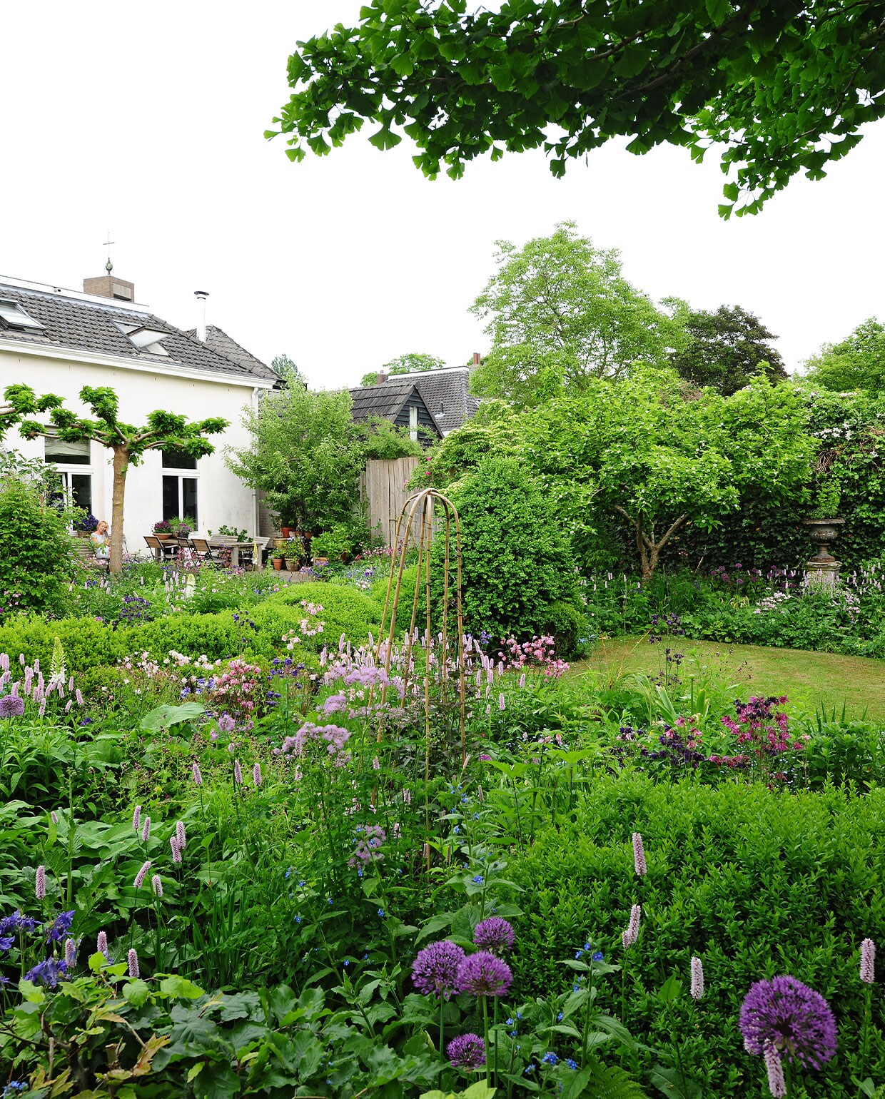 Binnen een patroon van breedbladige buxusplanten zette Miriam zo veel mogelijk bloemen neer. De betonnen sokkel met ijzeren sierpot stond al in de tuin toen ze het huis kochten. Tuintafel zelfgemaakt, herkomst stoelen onbekend.