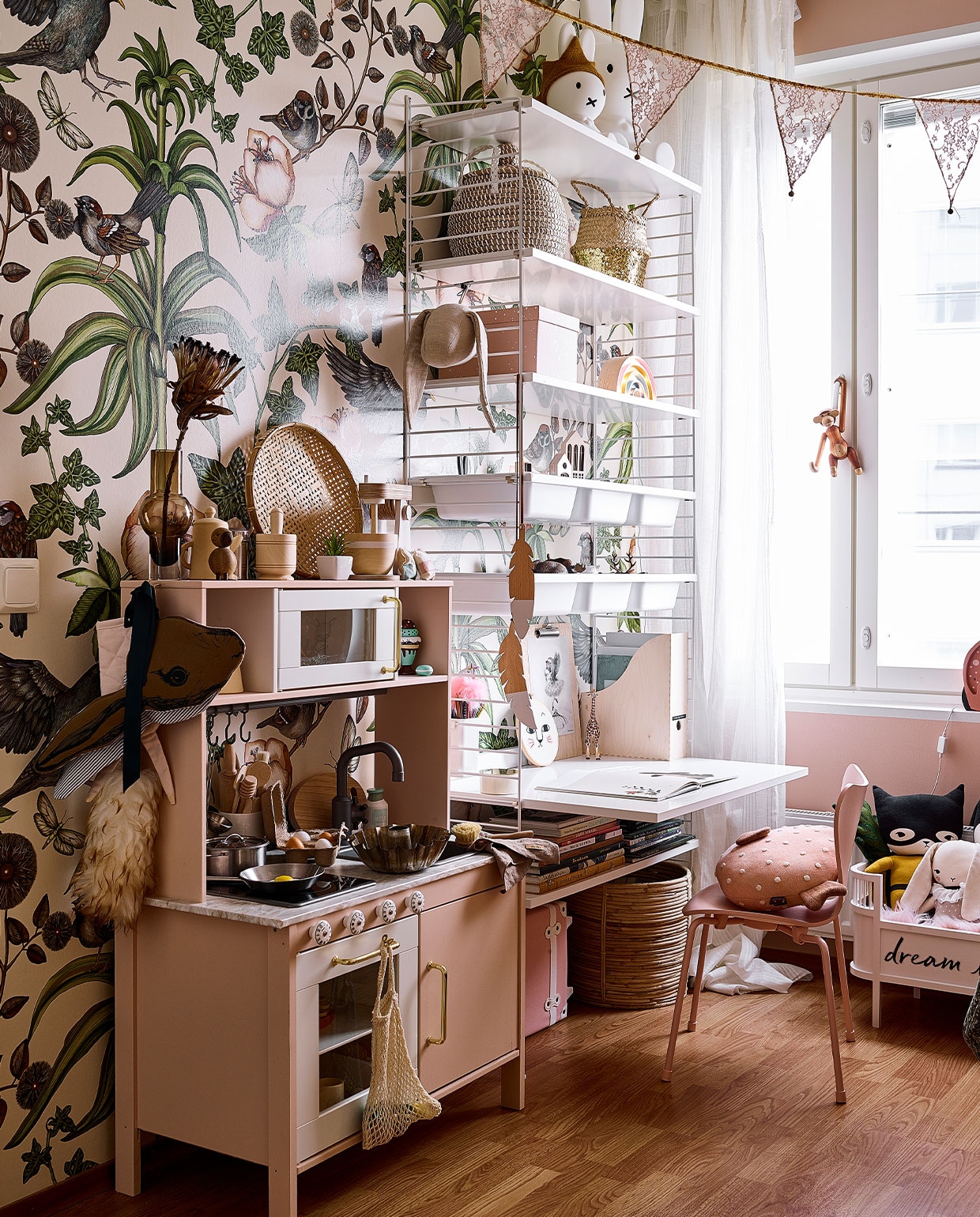 Vergelijkbaar behang Trending Wall en Studio Poppy. Wandrek String. Speelgoedkeuken Ikea, zelf geverfd en van nieuw blad en grepen voorzien. Cakevorm erfstuk. Vergelijkbare houten mixer Kids Concept, overig keukengerei onbekend. Nijntje-lampen De Winkel van Nijntje. Roze Vlinderstoel Mister Design. Aap van Kay Bojesen Vitra. Poppenbed Sebra. Superheldenknuffel en konijn Studio Bundis.