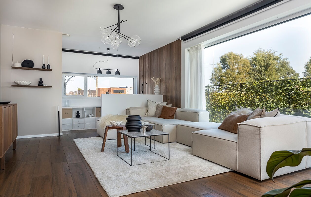 Tv-meubel, kast, dozen en gordijnen Ikea. Wandschap Woud. Schelpvormige schalen Loods 5, zwarte vazen en kandelaars Jysk en H&amp;M Home. Vierkante tafels Kwantum, houten kruk H&amp;M Home. Modulebank en lichte kussens Westwing, bruine kussens Kwantum. Kleed Tapeso. Lamp in zithoek Atmooz, lamp in leeshoek Lampen24. Witte vaas Jysk. Houten wand­panelen Maestro. Zonwerend rolscherm Sun Invest. Overig onbekend.
