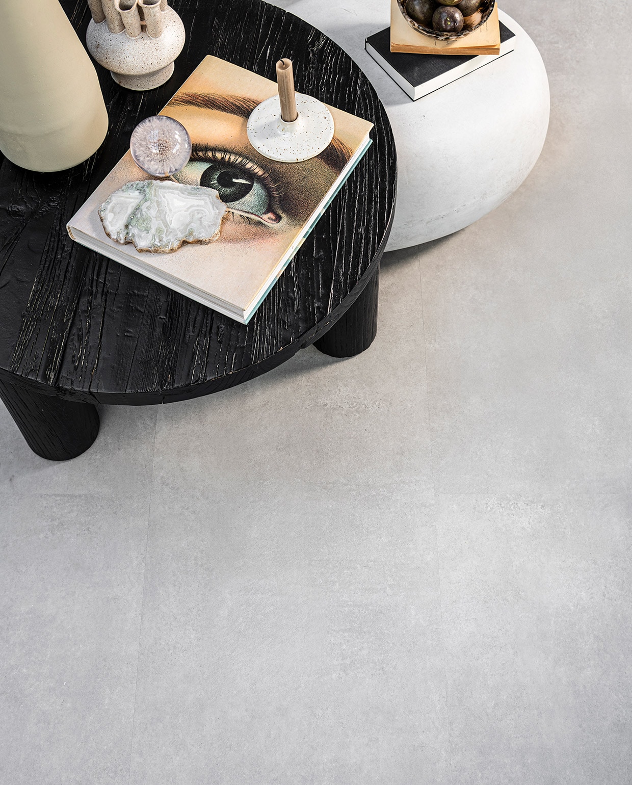 PVC Vloer Basic Light Grey, 91,4×45,7 cm, dryback per m² € 41,95, click per m² € 54,95.M.m.v. loods5.nl (zwarte salontafel van Loods 5 Goods), basiclabel.nl (bijzettafel Pebble betonlook van vtwonen), sissy-boy.com (zachtgroene vaas, vaas met meerdere halzen, kristal, gemarmerde kom), letoile.store (presse papier bloem, kandelaar). Overig privébezit.