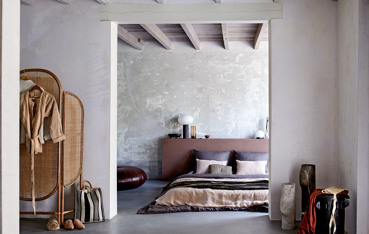 Kamerscherm, 180x130x3 cm (hxbxd), lamp met zwarte voet en witte bol (nordal.eu). Crèmekleurige jas van Fant, beige linnen blouse van Fant (sukha). Opgerolde linnen plaid, leren instappers, donkerbruin linnen dekbedovertrek met kussenslopen, 200×220 cm, bruine glazen waterkan (hm.com). Zwart-beige gestreepte shopper, beige nettas (maisonnl.com). Donkerbruine leren poef van Poltrona Frau, hoge marmerlook vazen prijs op aanvraag (covanderhorst). Hoofdbord geschilderd in verf kleur Tobacco, per liter (bauwerkcolour.com). Linnen dekbedovertrek in kleur Hazel vanaf, kussenslopen in kleur Hazel vanaf, linnen laken in kleur Sea Shell, 160×260 cm vanaf (bymolle.com). Donkerbruine plaid met beige patroon (homestede). Beige kussen met patroon van zwart zeegras (loods5). Zwarte zeepschaal op pootjes van Ferm Living, witte bollamp op marmeren ring van Ferm Living (vtwonen.be). Stuk koraal, hoge vaas (thingsilikethingsilove.com). Zwarte houten kruk Alila, 50×35 cm (hxØ) (casagitane.com). Overig privébezit.