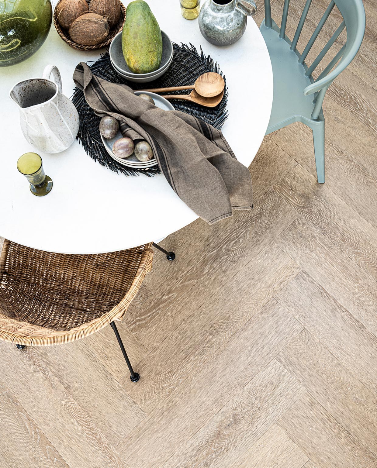 PVC Vloer Herringbone Sun Kissed, 76,5×15,3 cm, click 75×15 cm M.m.v. basiclabel.nl (eettafel en eetkamerstoelen van Woood), vtwonen.be (grijze borden, kommen, placemats, kruik met handvat, alles van Bloomingville), sissy-boy.com (grijze kan wit geverfd), hm.com (mand), paviljoennoord.com (groen wijnglas, groene waterglazen, houten bestek, groene glazen vaas, theedoek). Overig privébezit.