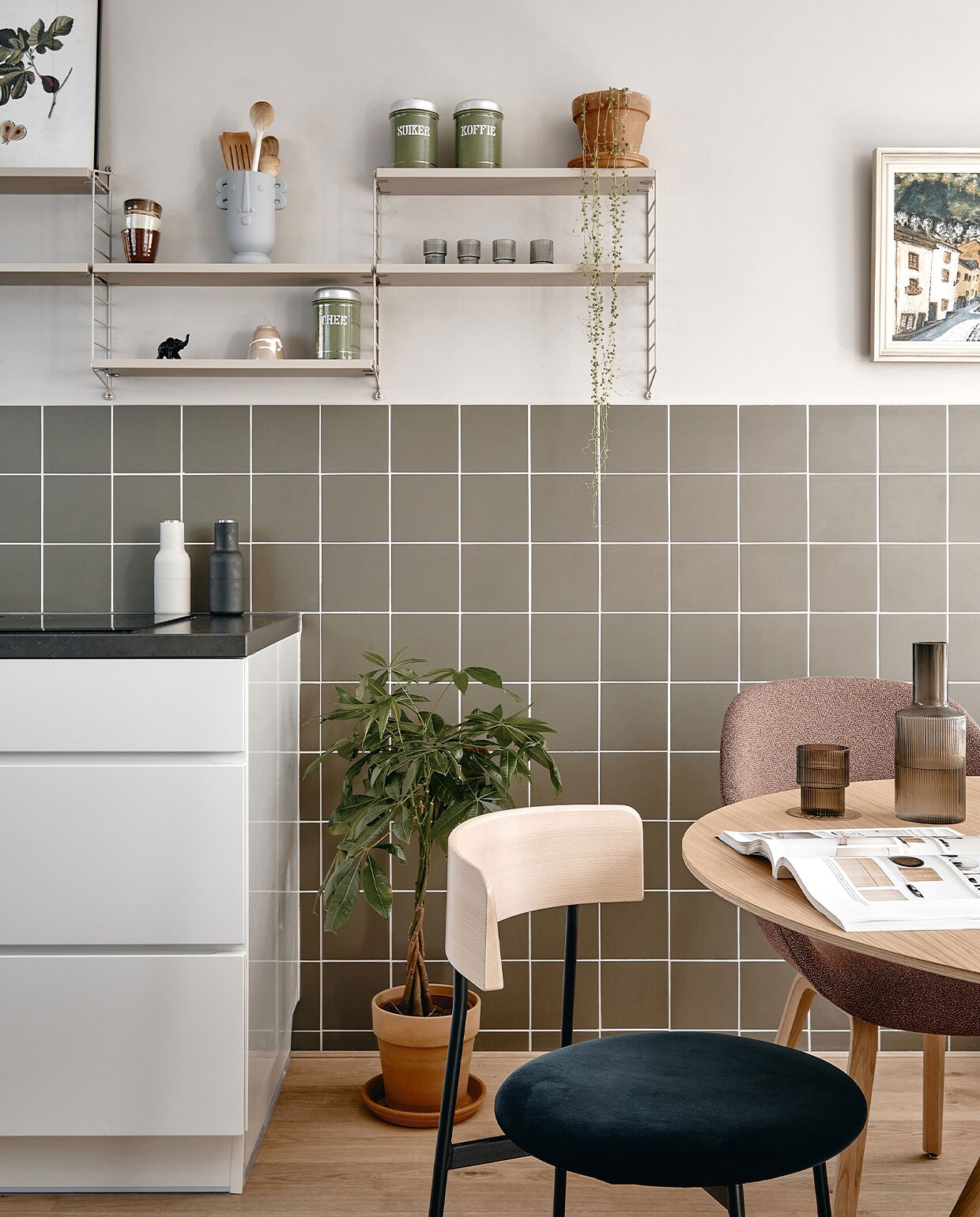 Muurverf Purbeck Stone van Farrow &amp; Ball. Wandtegels Winckelmans 15×15 cm in kleur Australian Green. Wandrek Pocket String Furniture, botanische print Junique, kopjes HKliving. Vaas cadeau gekregen. Voorraadbussen van Lindes overgrootmoeder. Peper-en-zoutstel Menu, plantenpotten Intratuin. Stoel links Friday in kleur Royal-56-petrol Fest Amsterdam. Stoel rechts About a Chair en eettafel Hay. Karaf en glazen Ripple van Ferm Living.