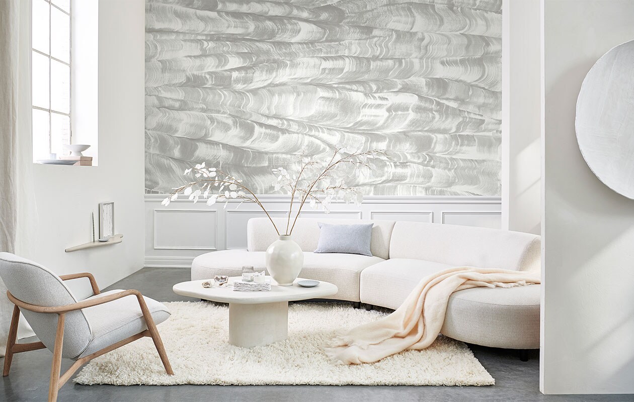 Paneelbehang Sand Waves uit de collectie Geo van Coordonné, per m2 vanaf € 60,- (van-sand.com). Kalkverf op wand kleur Lava White, vanaf 1 liter € 55,- (pure-original). Fauteuil € 2299,- (bolia.com). Gordijnen gemaakt van linnen stof Brera Lino van Designers Guild, prijs per meter € 86,- (wva). Vloerkleed van Linie Design € 715,- (vtwonen.be). Ovale schaal € 12,99 (hm.com). Schaal op voet € 44,95, vaas € 59,95 (urbannatureculture.com). Pleisterwerk wandplank € 140,- pleisterwerk salontafel € 640,- (velv). Blauwe gedraaide kaars, set van twee € 4,50 (paviljoennoord.com). Kunstwerk in lijst € 450,-, rond kunstwerk aan wand € 1100,- (julyadrichem.com). Bord € 19,90 (letoile.store). Bank, 187×155 cm (bxd) € 2295,- (loods5). Linnen kussen, vanaf € 39,- (bymolle.com). Wollen plaid € 119,- (zarahome.com). Overig privébezit.