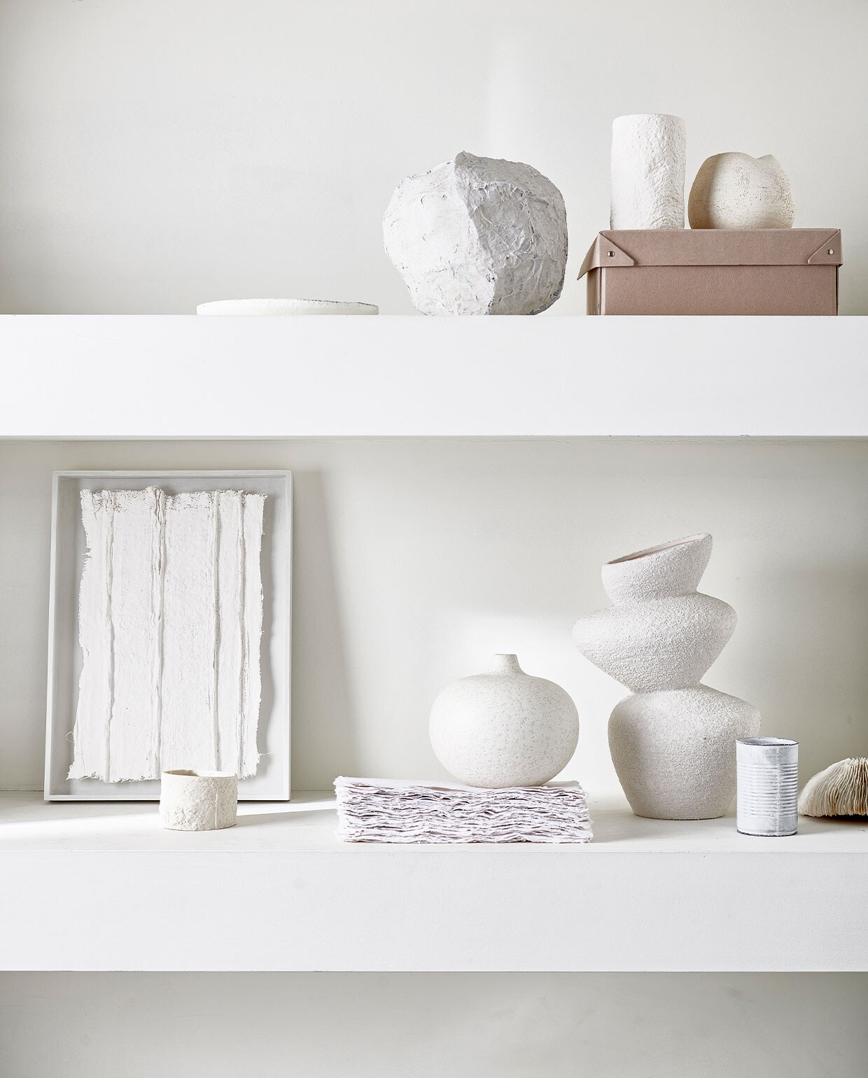 Bovenste plank van links naar rechts: mat wit bord € 12,99 (zarahome.com), papier-maché vaas prijs op aanvraag (julyadrichem.com), grove keramieken pot € 12,99 (zarahome.com), witte keramieken bolvaas € 95,- (annemiekebootsceramics.nl). Onderste plank van links naar rechts: kunstwerk in lijst € 450,- (julyadrichem.com), keramieken mok € 22,90, witte bolvaas € 49,99 (letoile.store), grove keramieken vaas € 29,99 (hm.com). Overig privébezit.