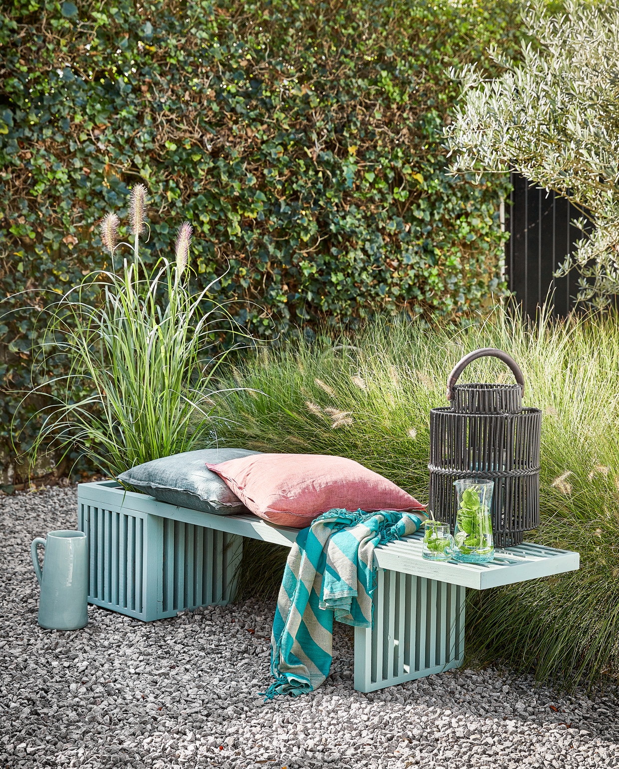 Lichtblauwe waterkan € 42,50 (loods5). Linnen kussens € 49,95 per stuk (nijhof-baarn). Gestreepte plaid Candy Stripe € 34,99 (sissyboyhomeland.com). Zwarte tuinlantaarn Bartolone € 139,-, grijze plantenbak in de bank € 29,99 (intratuin). Glazen karaf € 17,95, glas met oor € 3,95 (householdhardware)