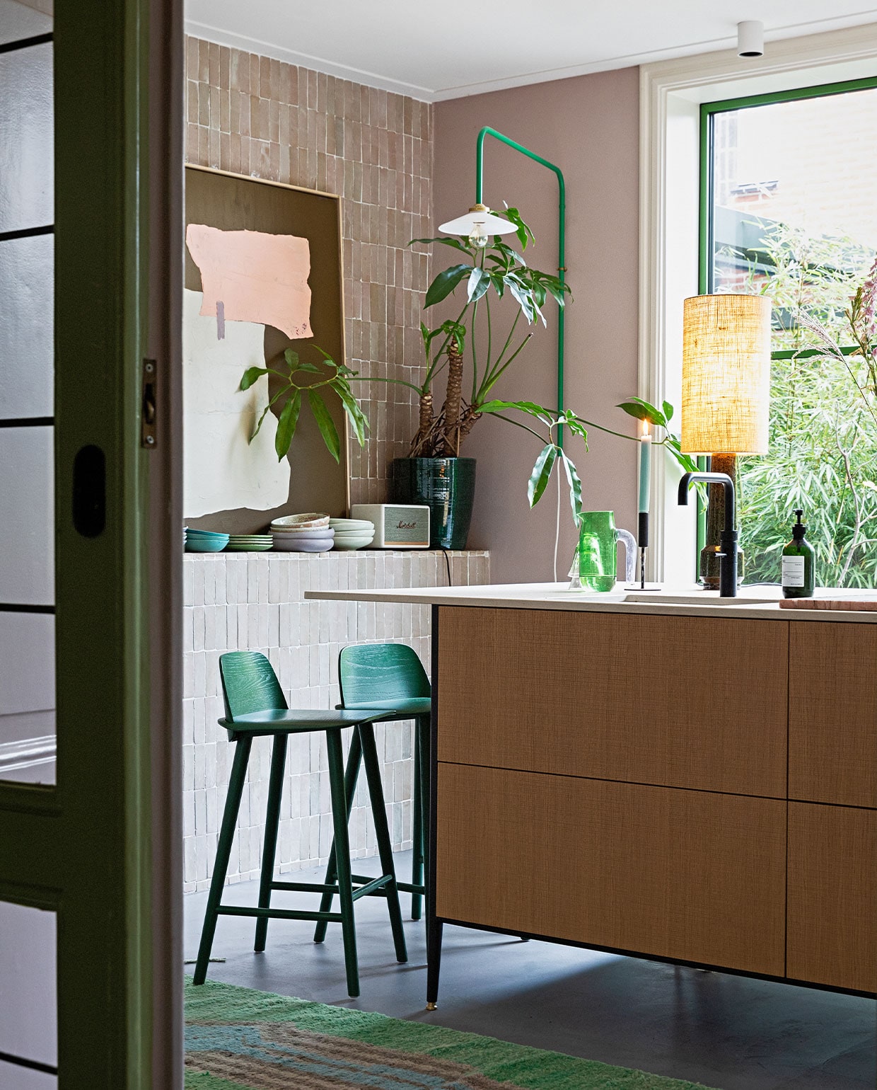 Groene lamp aan muur Valerie Objects. Tegels Bejmat Gris rose Marokkaanse tegels via Design Tegels. Schemerlamp en kunst HKliving. Kandelaar Hema. Kan Hay. Plantenpot Serax. Muziekbox Marshall. Servies mix van onder andere Home Chef en 70’s ceramics van HKliving. Krukken Nerd van Muuto. Keuken Unit van Cesar Kitchens. Kleed vintage berber. Aluminium pui in kleur Varen Groen. Lamp plafond onbekend.