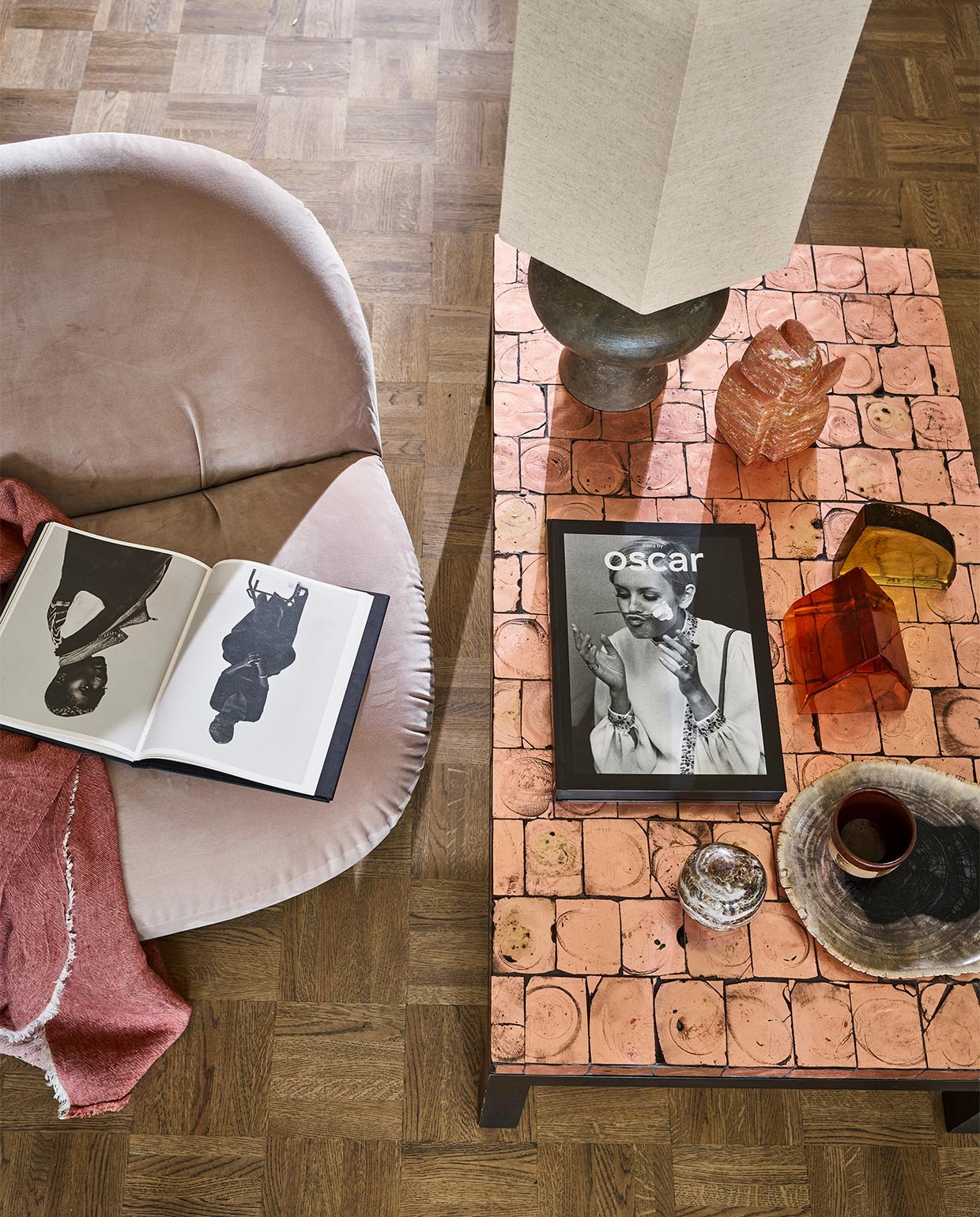 Fauteuil van Pierre Paulin voor Gubi (neeflouis.nl). Linnen plaid (couleurlocale.eu). Schemer- lamp, voet, kap, oranje glasobject, geel glasobject (hkliving.nl). Travertin beeld Wachter van Mirjam de Nijs, prijs op aanvraag (beeldenvansteen.nl). Salontafel, 111x62x34 cm (vintagehoarder.com). Boekop tafel Icons by Oscar (lannoo.be).