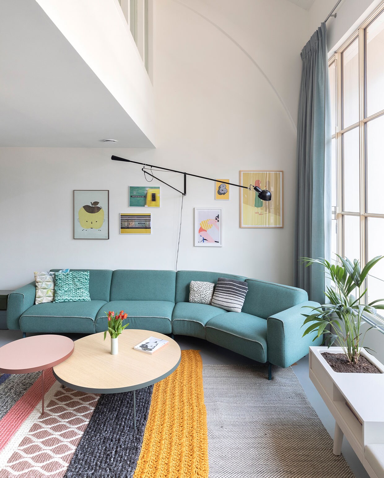 Hoekbank Melloo van Pode, raambank Level 34 van Vitra, ronde koffietafels Gau van Treku. Groot tapijt Moiré Kelim van Hay, gebreid tapijt Mangas MR2 van Gan Rugs. Wandlamp 265 van Flos, gordijnen Combo Design, stof van De Ploeg, kussens Snurk en Kidscase Home. Kunstwerken: meisje met schaduw Girl van Stephan Schmitz, Apple Papple poster van Fine Little Day, twee foto’s van metrohalte Alexanderplatz in Berlijn: Liebesbeweis en Reaching Alex van Michael Belhadi, &amp;-teken van The Motivated Type via Juniqe, fietsster Bike van Céleste Wallaert via Juniqe.
