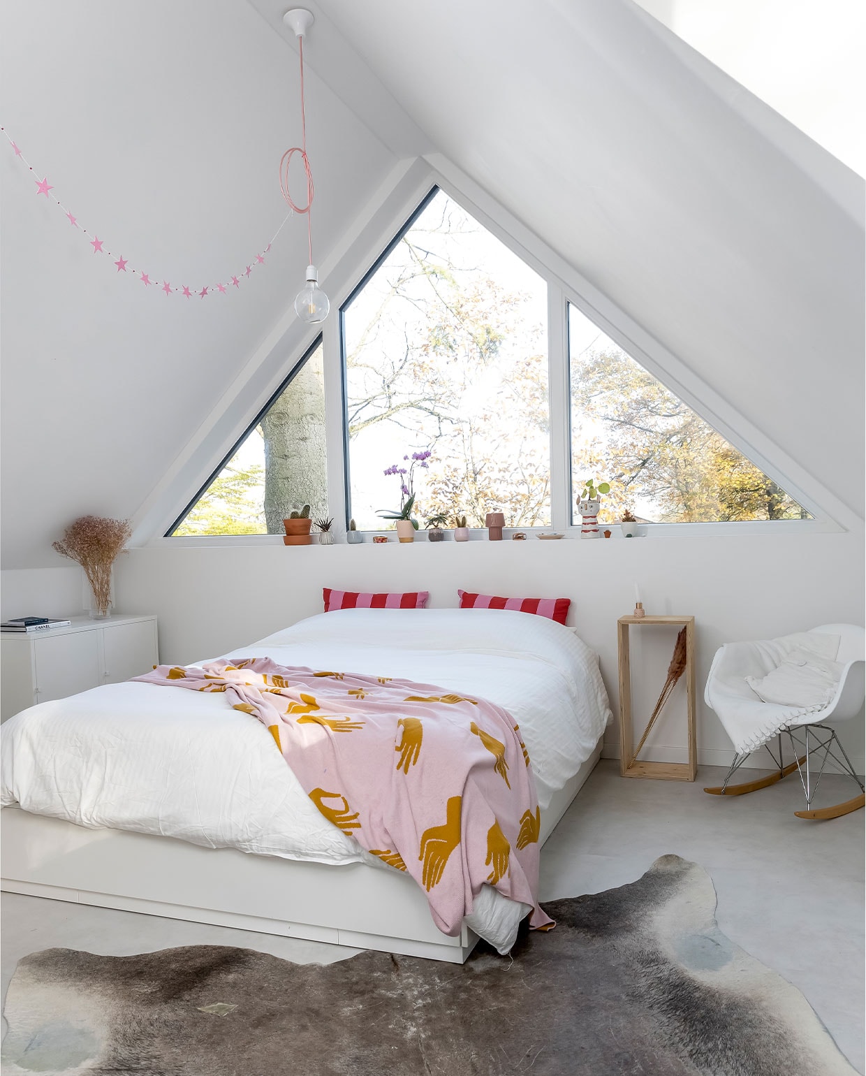 Kleed Marktplaats, kast, witte sprei en kussens Ikea, stoel Vitra, roze sprei Sissy-Boy, nachtkastje zelfgemaakt, plantenpotten Loods 5, vaas met droogbloemen Hema, lamp Snoerboer, slinger Jansje.
