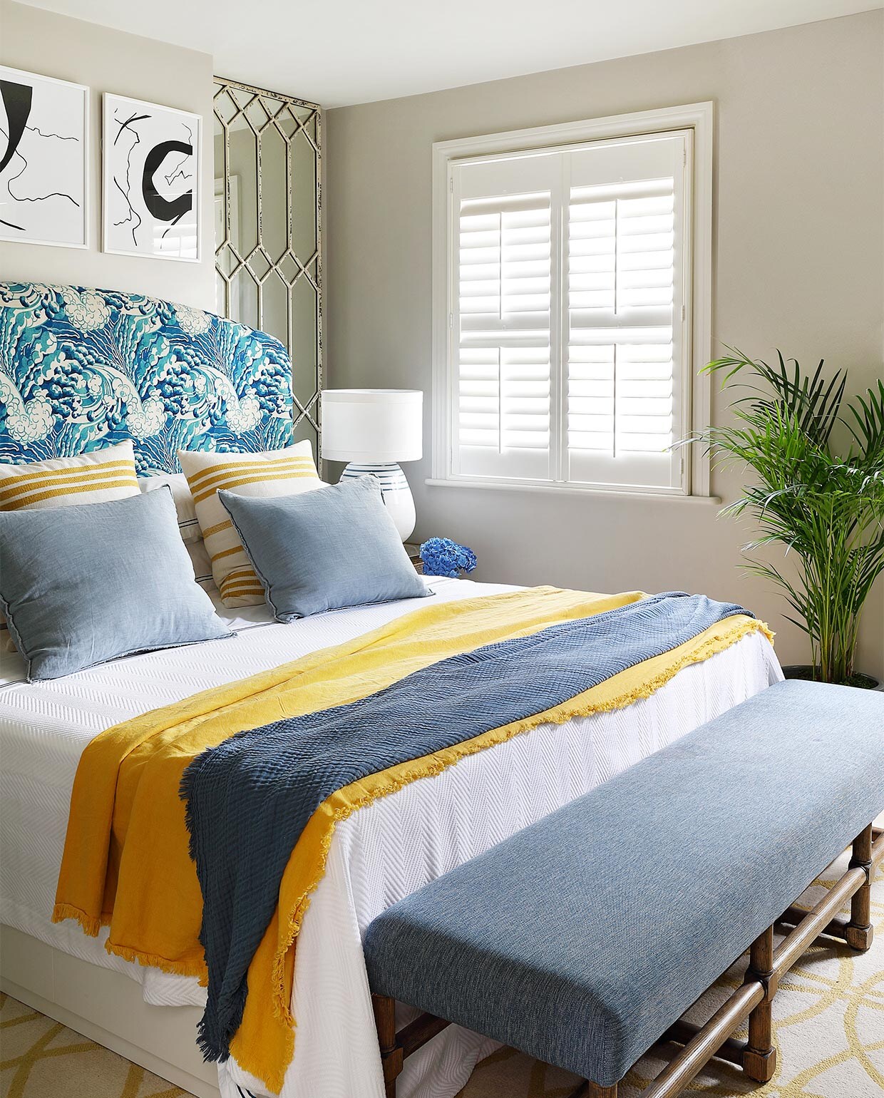 Muurverf Cornforth White van Farrow &amp; Ball. Het hoofdbord is bekleed met stof The Wave in de kleur mineral van Linwood Fabric. Beddengoed Granny Goose. Kussens met gele streep van stof Marina in kleur pastis van Lelièvre. Vaalblauwe linnen kussens lokaal gekocht. Gele en blauwe plaids H&amp;M Home. Spiegel Block &amp; Chisel. Tafellamp Gioalo van OKA. Bankje bekleed met stof van Mavromac. Kunst in lijsten gekocht via Etsy.
