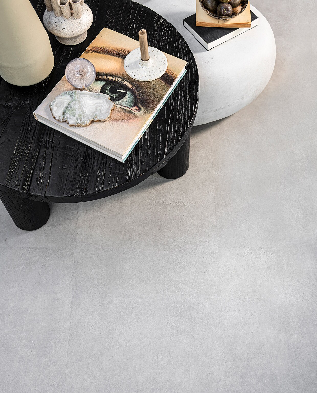 PVC Vloer Basic Light Grey, 91,4×45,7 cm, dryback per m² € 41,95, click per m² € 54,95. M.m.v. loods5 (zwarte salontafel van Loods 5 Goods), basiclabel (bijzettafel Pebble betonlook van vtwonen), sissy-boy.com (zachtgroene vaas, vaas met meerdere halzen, kristal, gemarmerde kom), letoile.store (presse papier bloem, kandelaar). Overig privébezit.