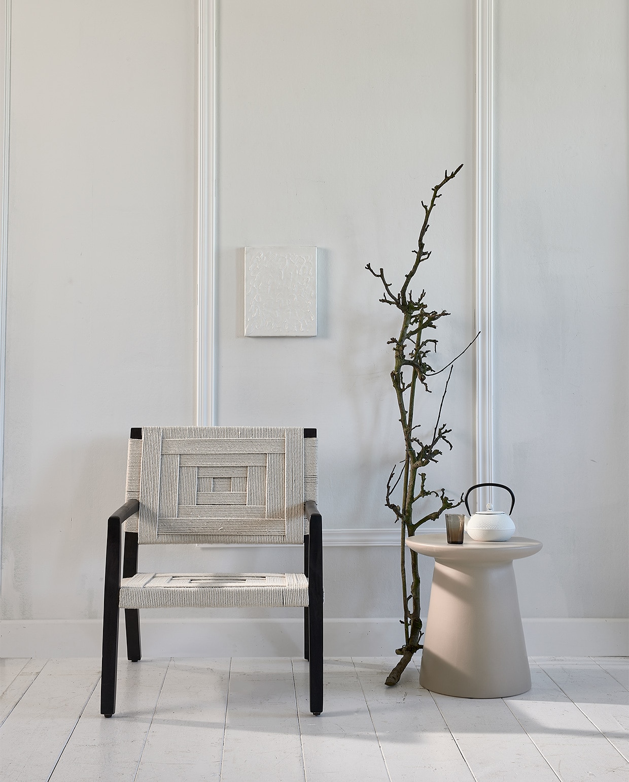 Stoel met gevlochten singels Shima (eijerkamp). Keramische tafel (hkliving). Japanse theepot, grijs geribbeld glas, (loods5.nl). Kunst prijs op aanvraag (atolty.com). Lijsten via bouwmarkt.