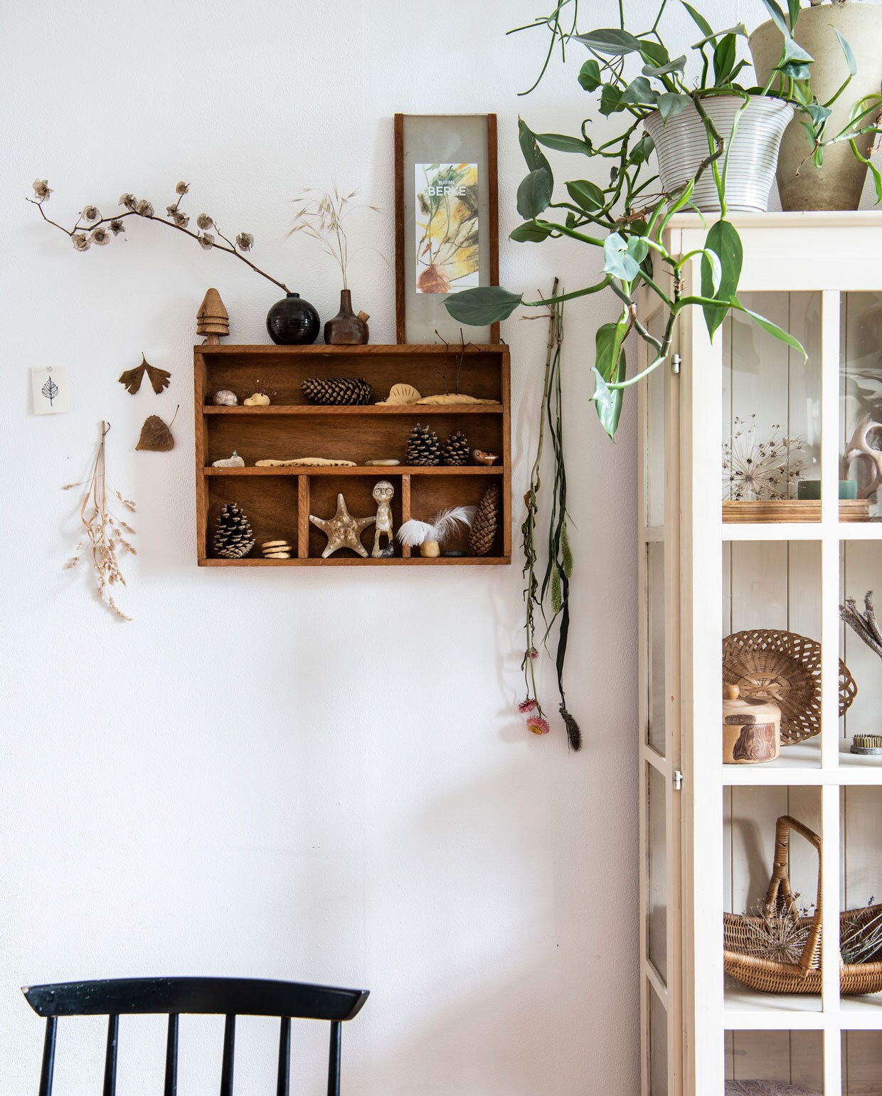 Vitrinekast via kennis, letterbak tweedehands. Planten Ficus benghalensis, Philodendron silver sword, potloodcactus, pannenkoekplant. Tafel en gevlochten mand tweedehands, Farstrup-spijlenstoelen Hit &amp; Run. Lamp zelfgemaakt van visnet, zwarte vaas D&amp;M Deco, kandelaar Rustik Lys.