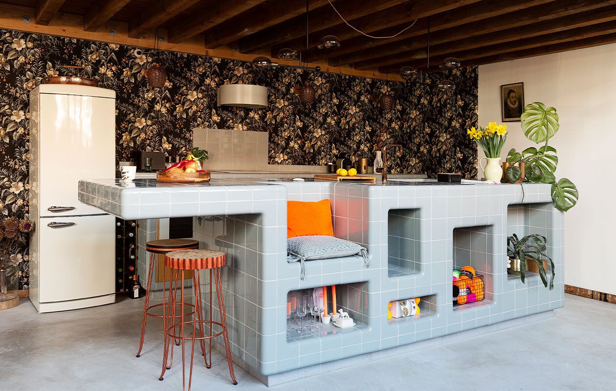 Keuken van D-tile in de kleur Duif. Kookplaat, afzuigkap en oven Ikea, kraan van Nivito, ­afneembaar behang Hornbach, lampen Tangle via made.com, barkrukken Kave Home.