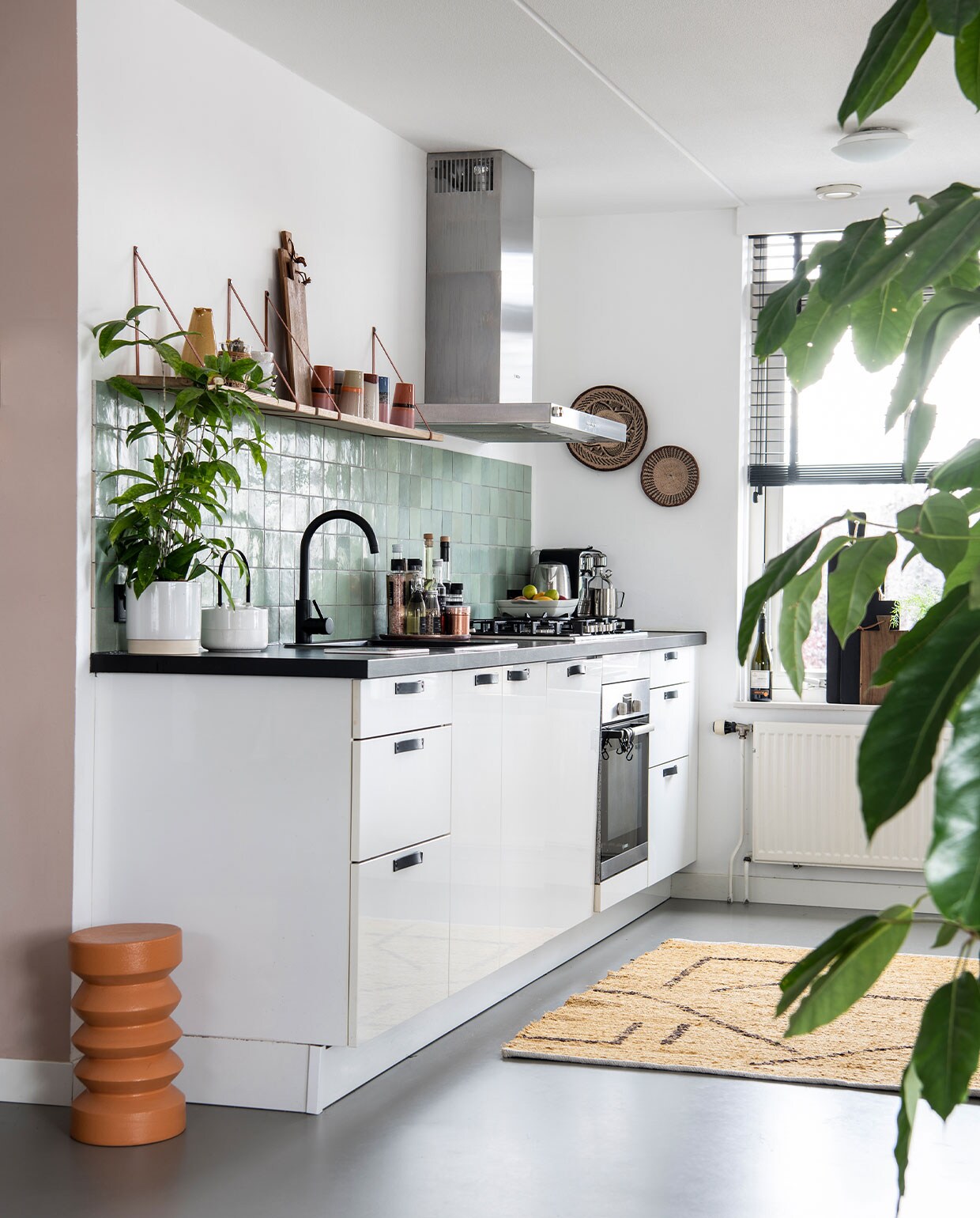 Muurkleur Zeester van Flexa, gietvloer Evolve. Tegels Jan Groen, keuken vorige bewoner, leren handgrepen en eiken- houten plank van Handles en more, oranje bijzettafel, houten planken, kleed en latte mugs HKliving, vaas Sissy Boy. Plantenpotten Gina Da, wanddecoratie uit Afrika. Raambekleding Ilumio.