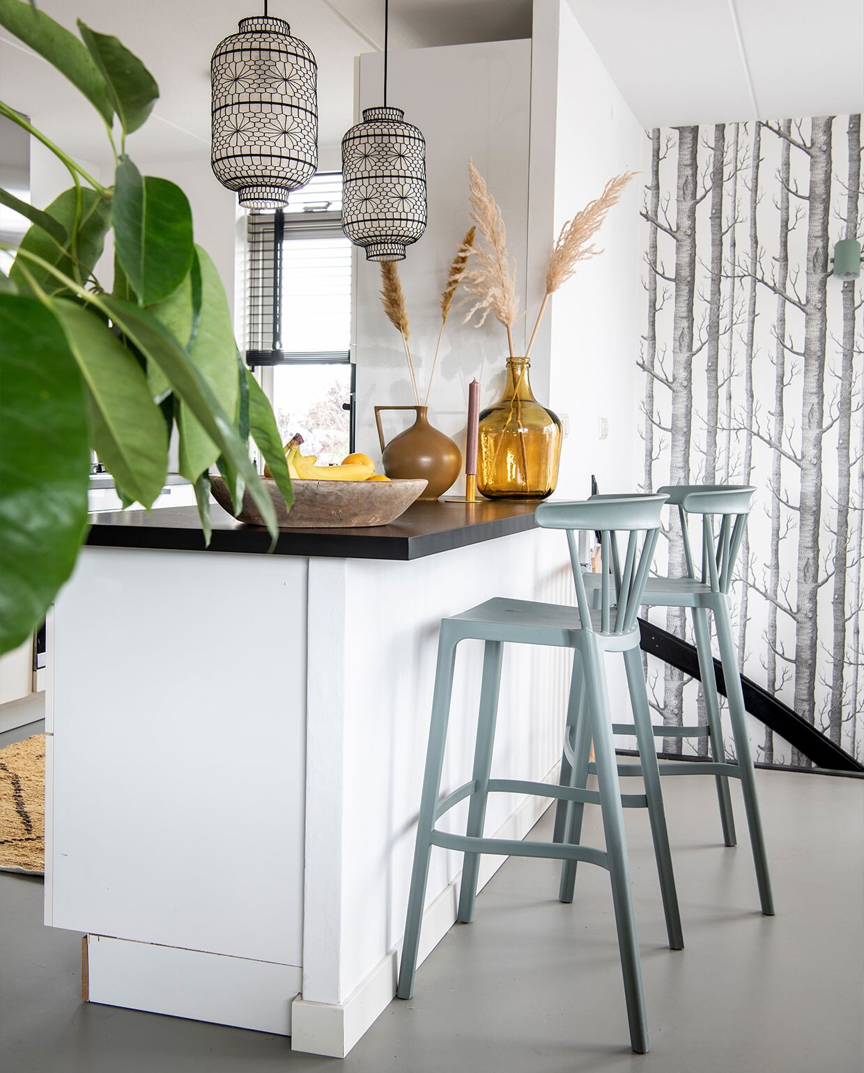 Barstoelen Woood, vloerkleed en gele vaas HKliving, gietvloer Evolve, keuken vorige bewoner, lampen Dutchbone, behang Cole and Son. Fruitschaal Raw Materials, kandelaar Branded, kaarsen Rustik. Bruine vaas onbekend.